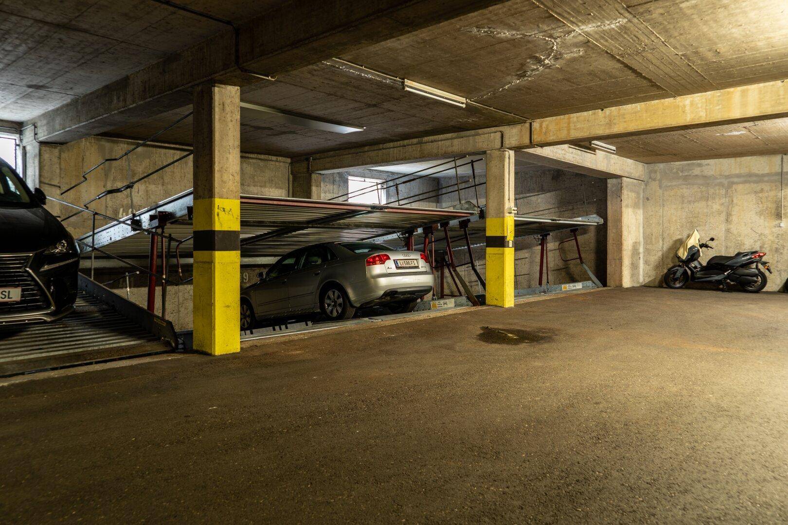 Tiefgarage mit Doppelparker-System, zwei Autos und einem Motorrad in einer Betonkonstruktion.