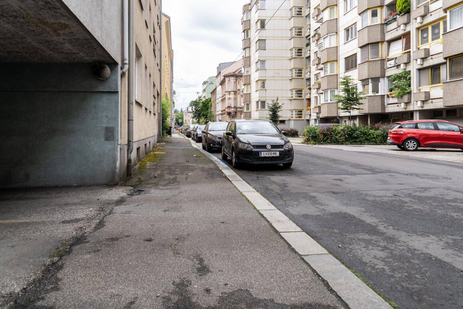 Seitenansicht der Straße mit Gebäuden und parkenden Fahrzeugen am Straßenrand.