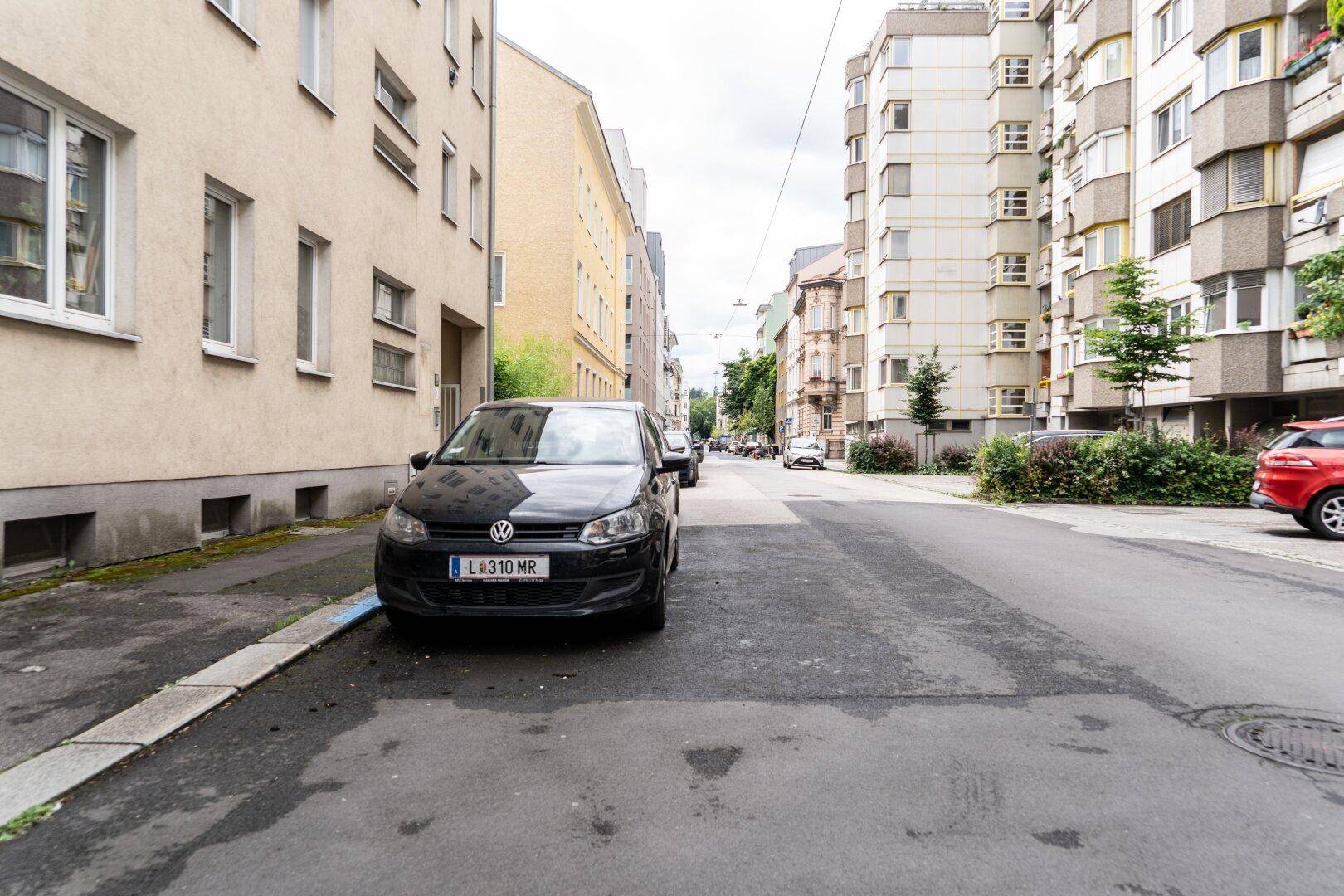 Straßenansicht mit Gebäuden und einem geparkten Auto am Bordstein.