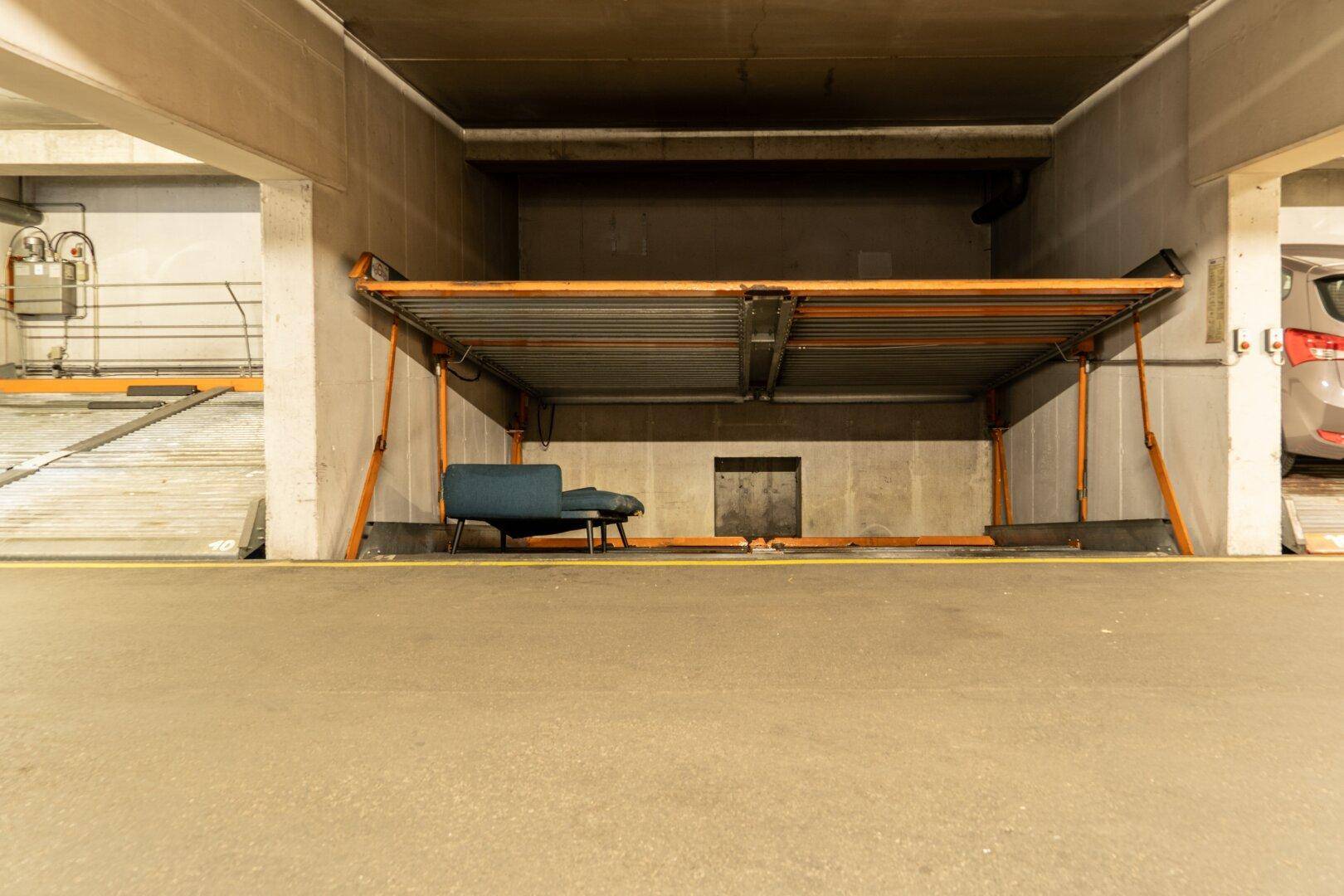 Detailansicht des automatischen Parksystems in der Tiefgarage mit einem blauen Stuhl und Betonboden.