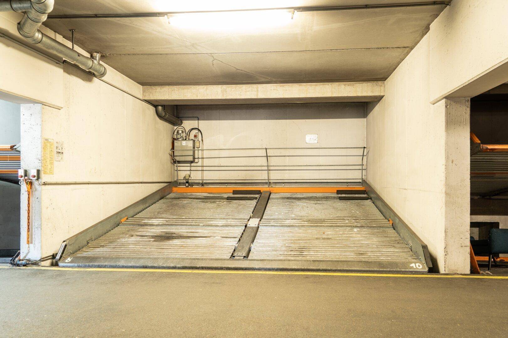 Einfahrt zum automatischen Parksystem in der Tiefgarage mit gelber Markierung und Rohren an der Decke.