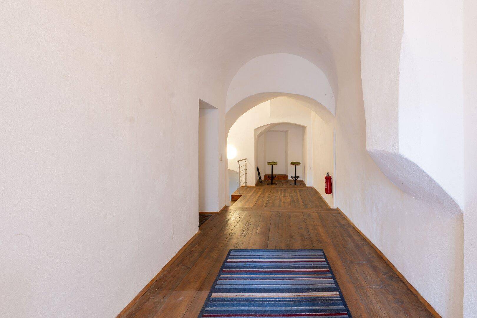 Langer Flur mit Holzdielenboden, weiß getünchten Wänden und gewölbter Decke.