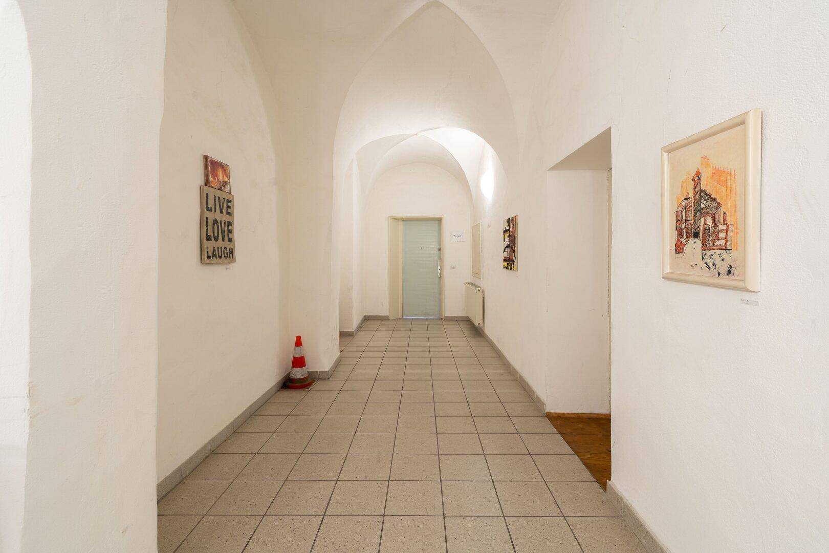Langer Flur mit Fliesenboden, weiß gestrichenen Wänden und gewölbter Decke.