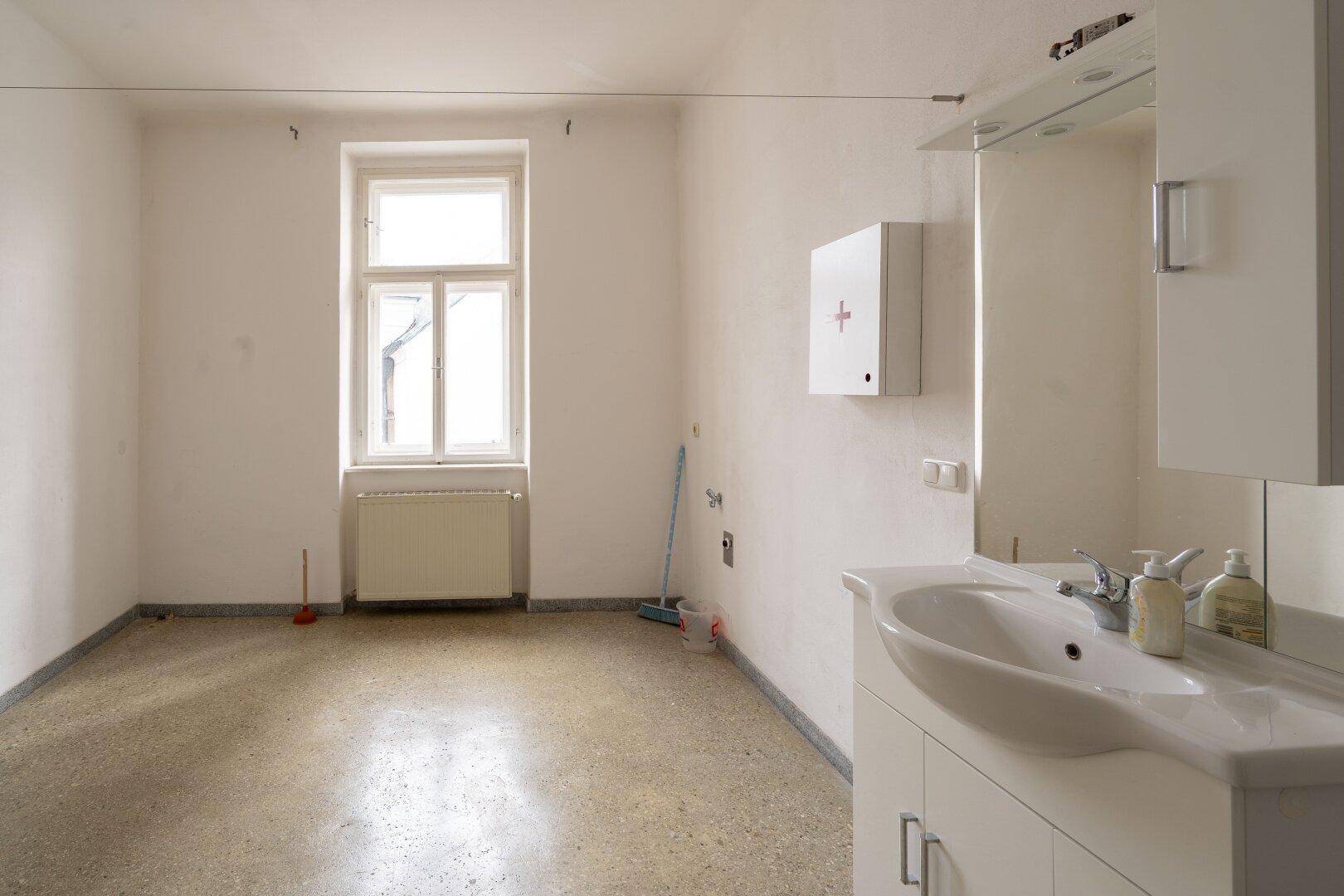 Heller Raum mit Waschbecken, Spiegelschrank und Fenster, bereit für die Einrichtung.