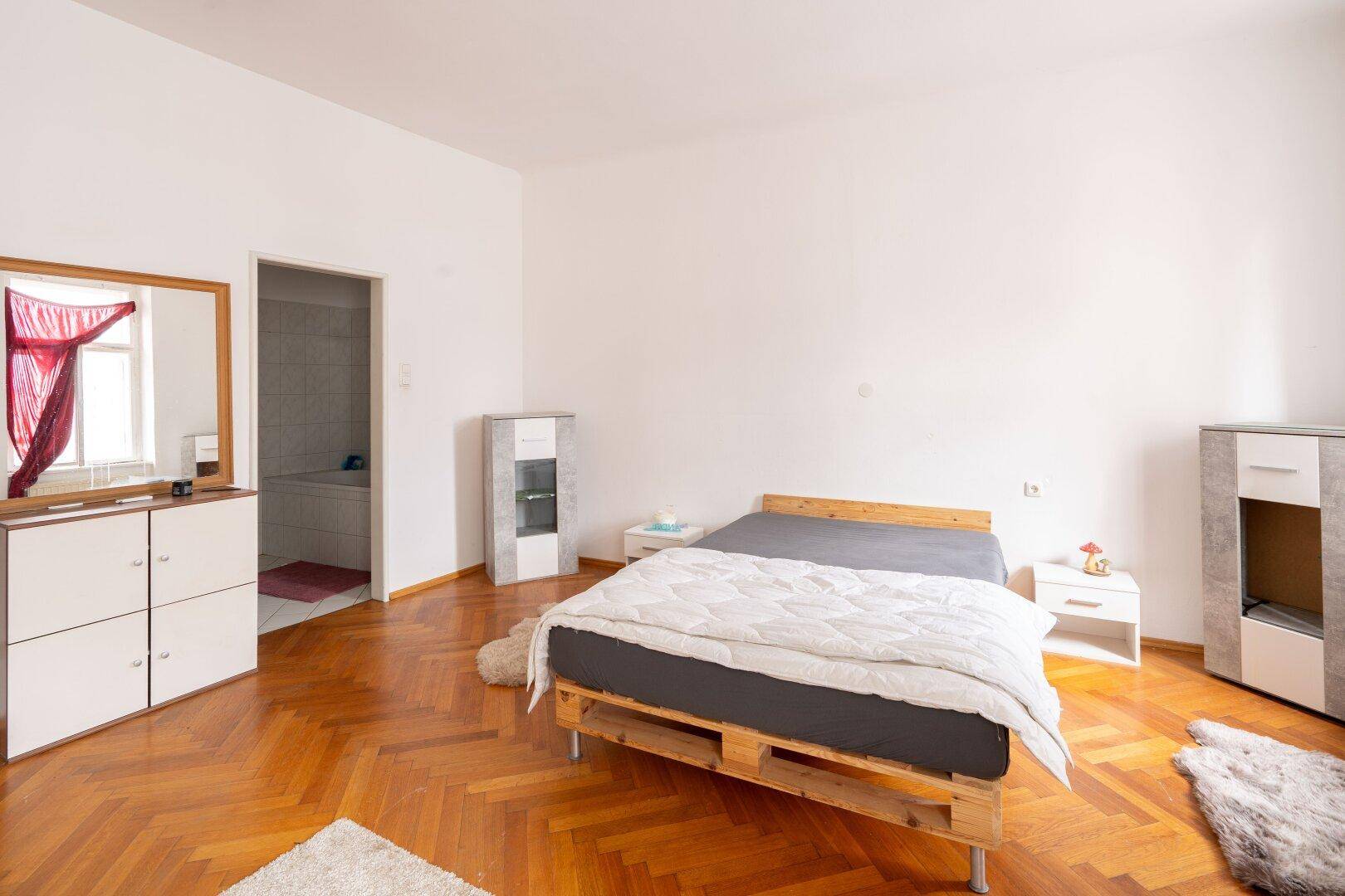 Schlafzimmer mit Parkettboden, Doppelbett und Zugang zu einem angrenzenden Badezimmer.