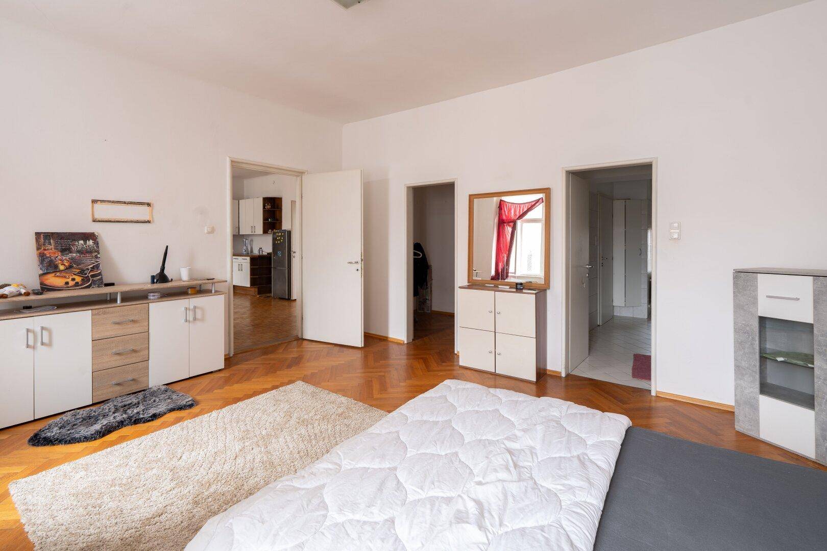 Geräumiges Schlafzimmer mit Parkettboden, Bett und mehreren Türen zu anderen Räumen.