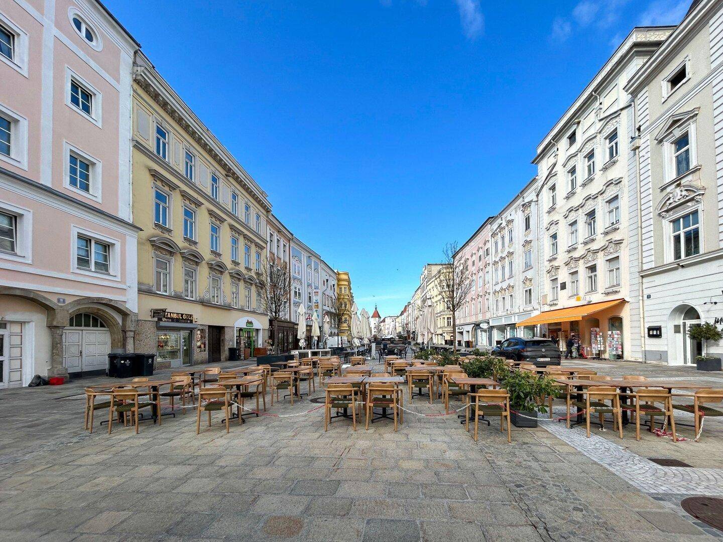 Weitläufige Straßenansicht mit historischen Gebäuden und einer Außenterrasse mit vielen Tischen.