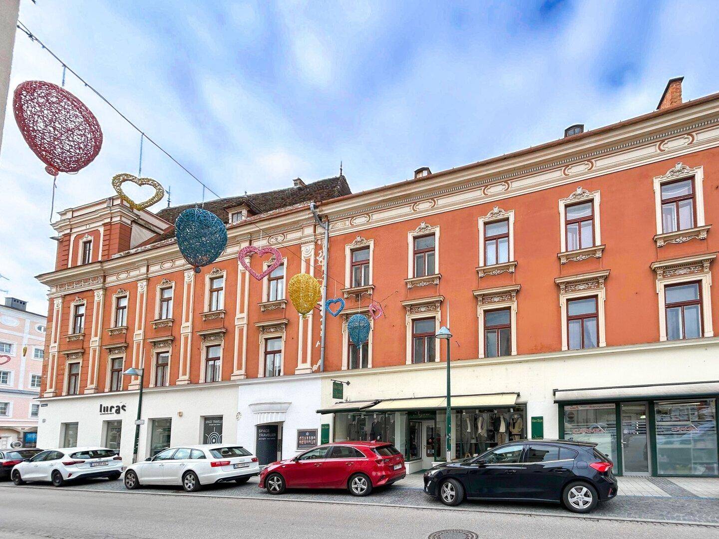 Historisches Gebäude mit orangeroter Fassade und Geschäften im Erdgeschoss, geschmückt mit bunten Herzen.