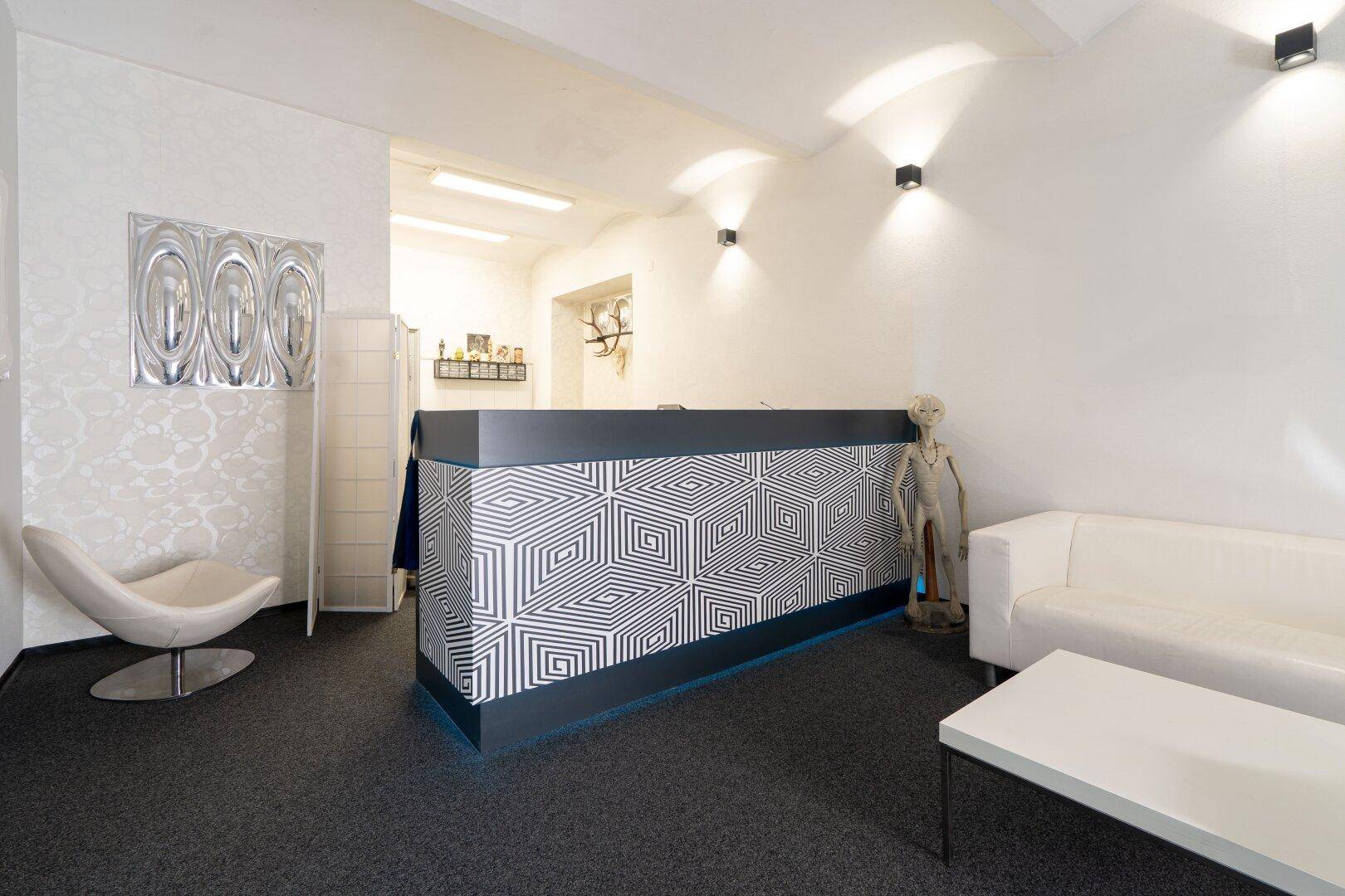 Moderner Empfangsbereich mit auffälligem Tresen, weißem Sofa und dunklem Teppichboden.