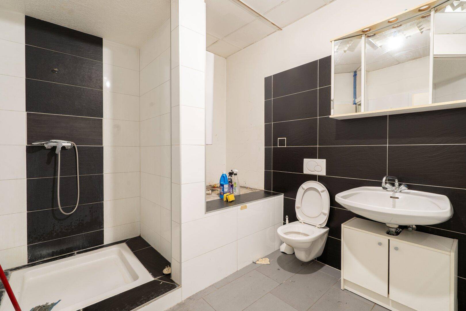 Modernes Badezimmer mit Dusche, WC und Waschbecken, in Schwarz-Weiß-Fliesen gehalten.