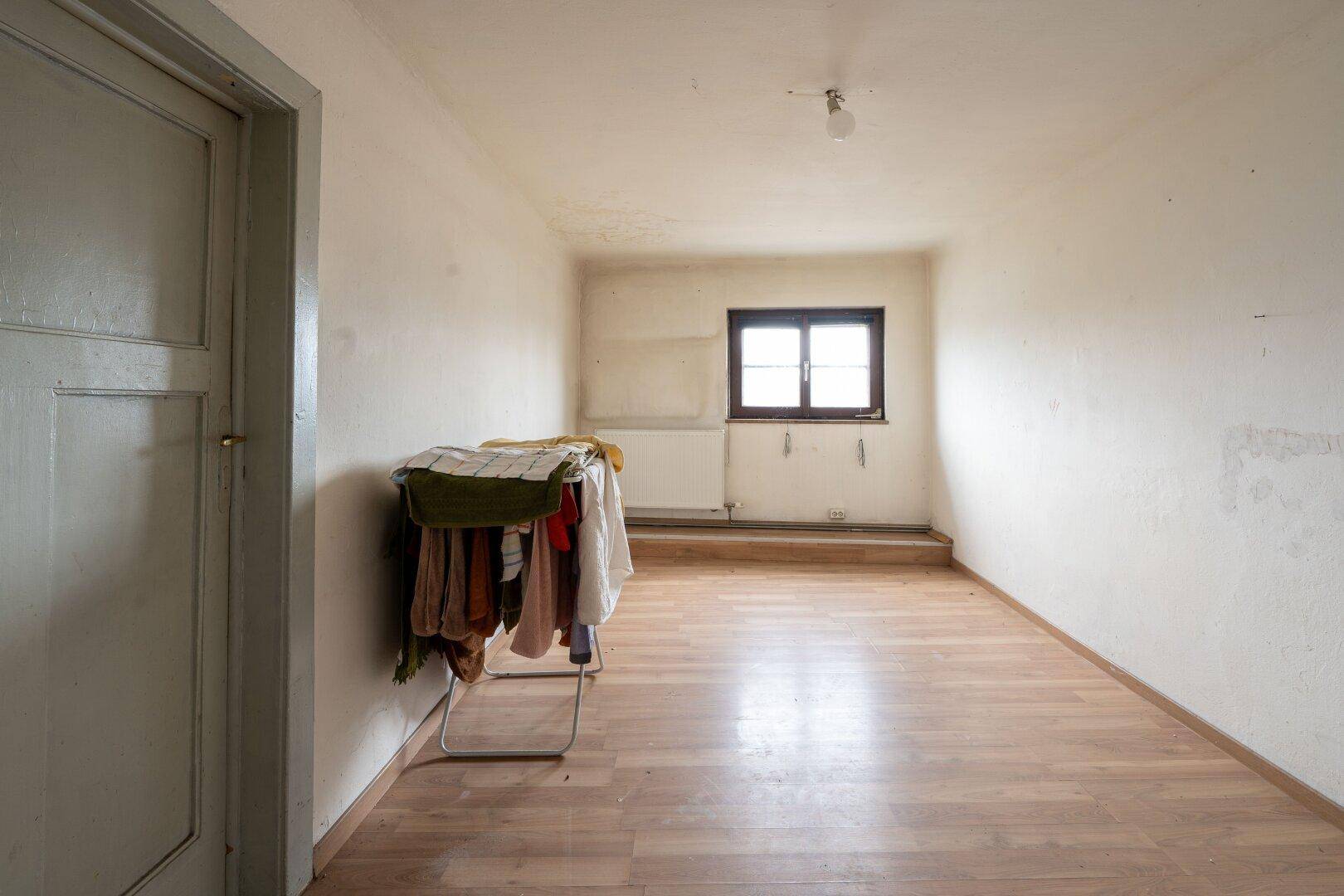 Leeres Zimmer mit Laminatboden und einem Fenster, das auf die Umgebung blickt, in schlichtem Design.