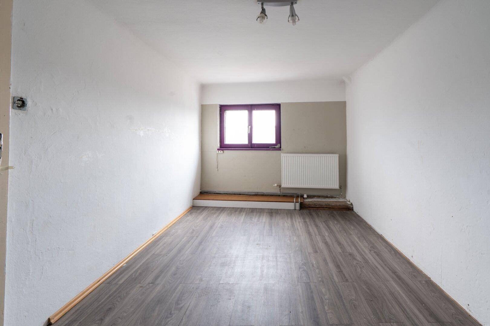 Heller Raum mit Laminatboden und einem Fenster, vielseitig nutzbar als Büro oder Schlafzimmer.