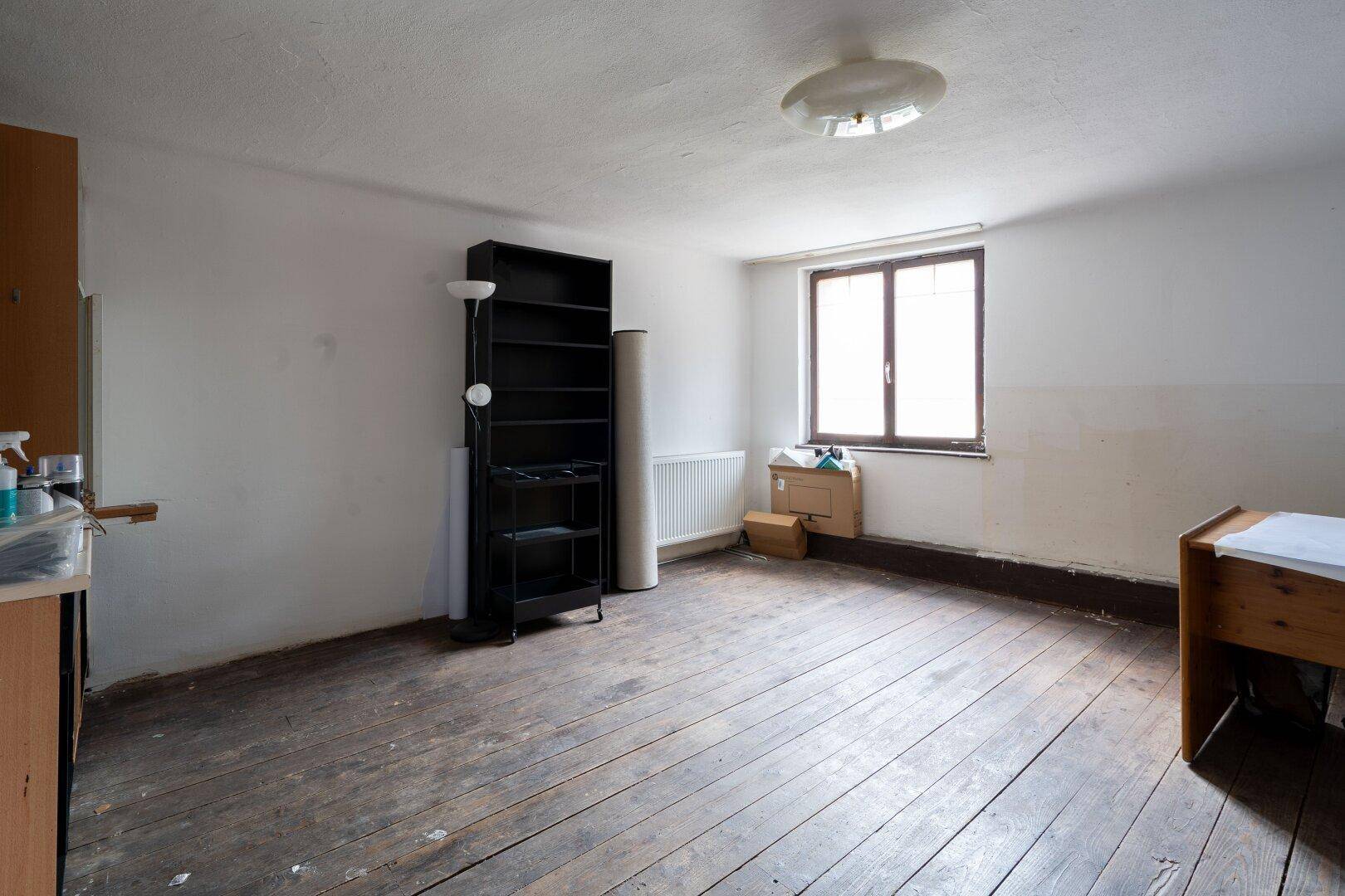 Geräumiges Zimmer mit altem Dielenboden und einem großen Fenster, das viel Licht spendet.