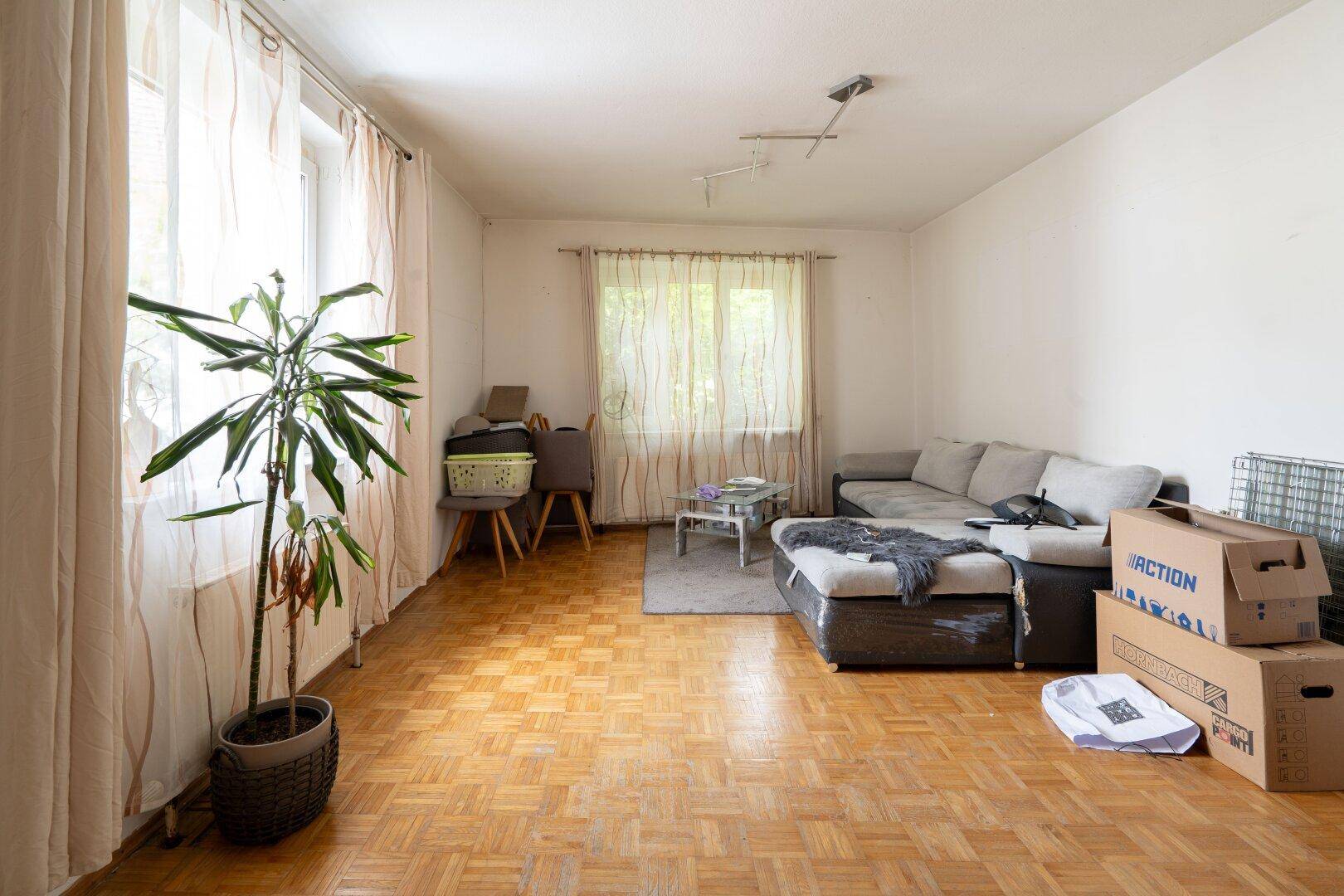 Gemütliches Wohnzimmer mit Fischgrätparkett, Sofa und großen Fenstern für viel Tageslicht.