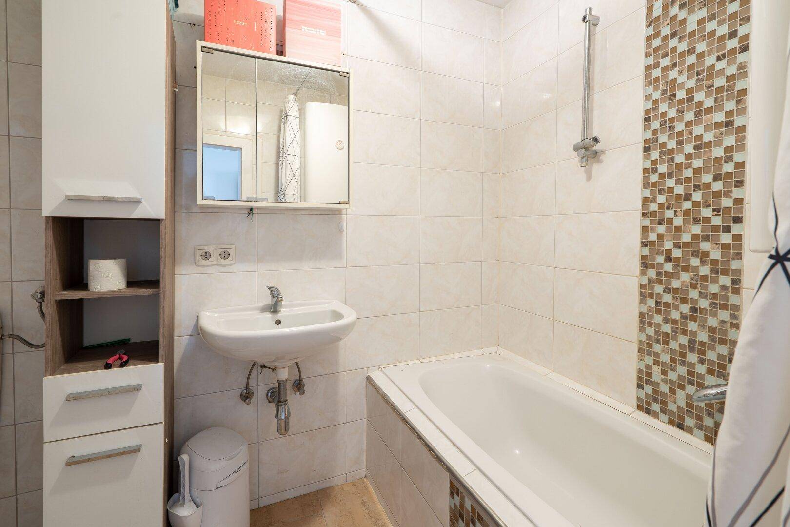Gefliestes Badezimmer mit Badewanne, Waschbecken und Spiegelschrank, in hellem und funktionalem Design.