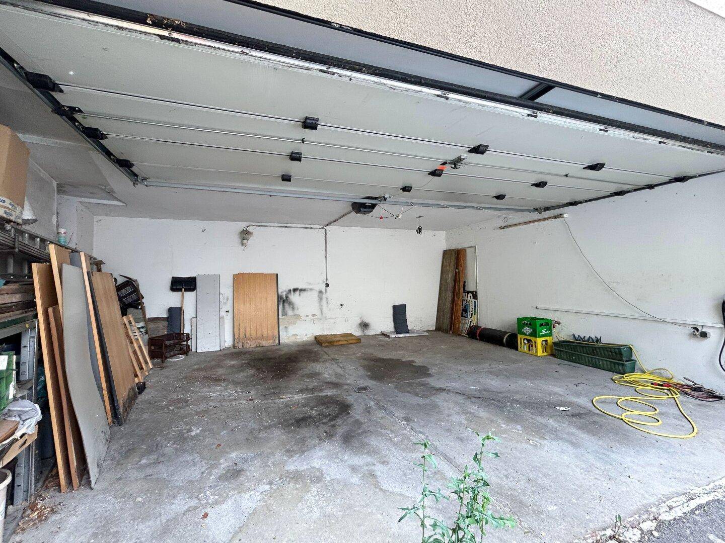 Geräumige Garage mit Betonboden und viel Stauraum, ideal für Fahrzeuge und Lagerung.