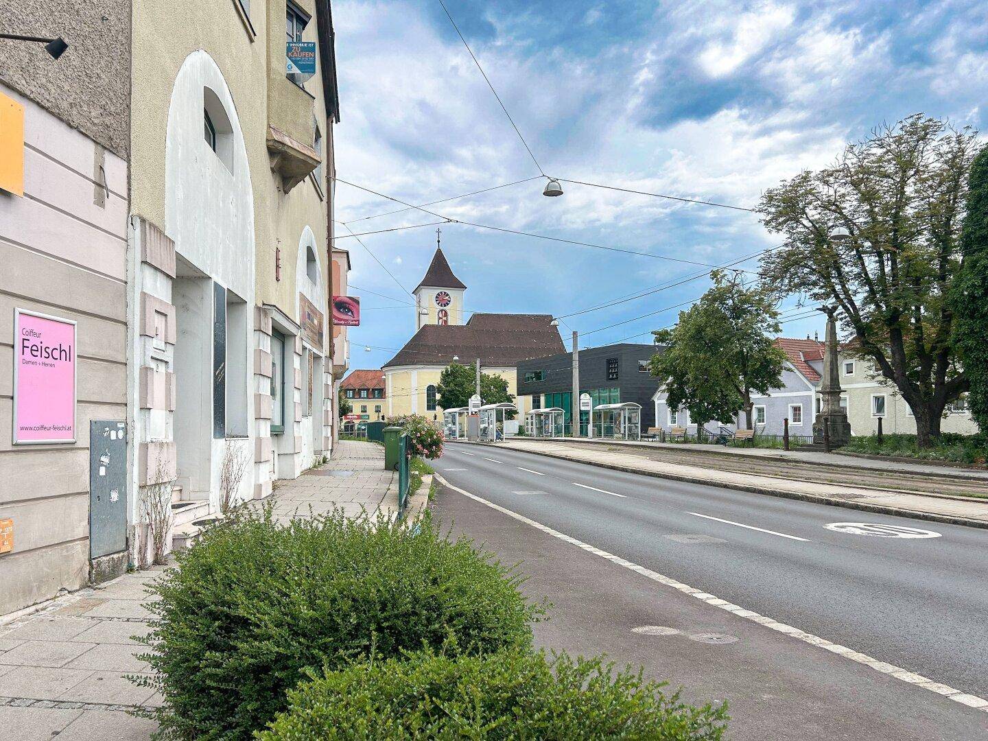 Straßenansicht mit historischen Gebäuden, einer Kirche im Hintergrund und einer Straßenbahnhaltestelle.