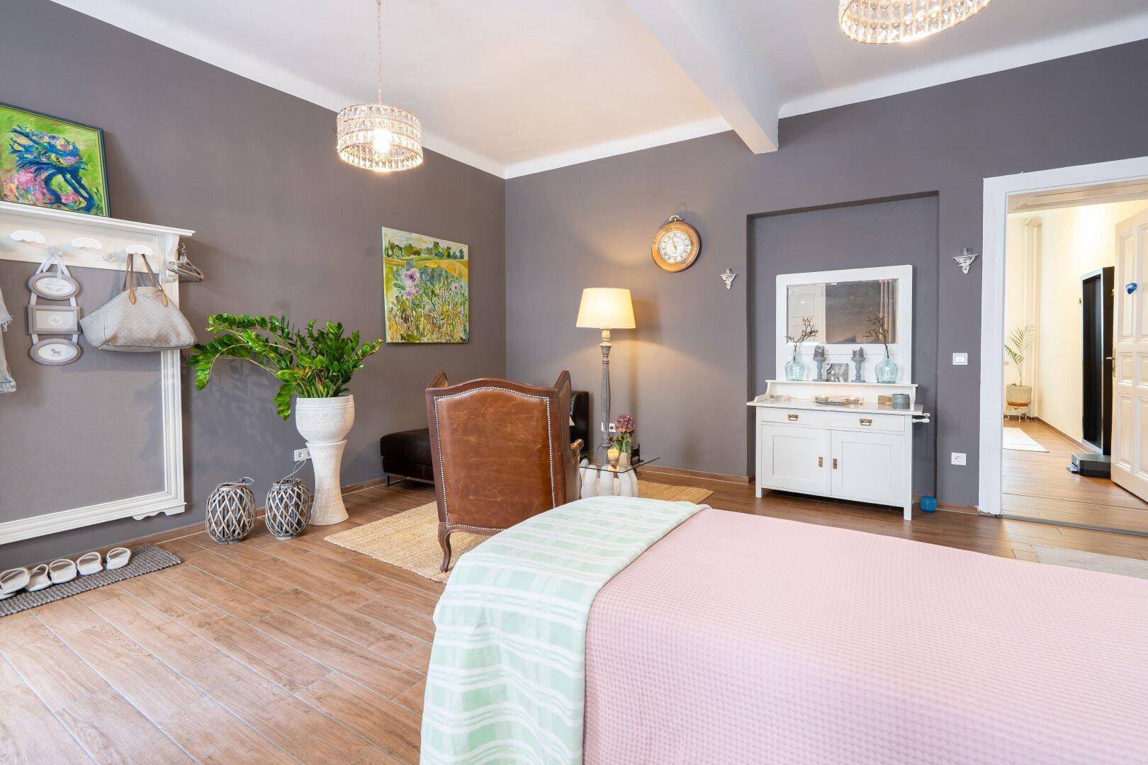 Helles Wohnzimmer mit grauen Wänden, Holzboden und stilvoller Einrichtung, inklusive Kronleuchter und dekorativem Kaminmantel.