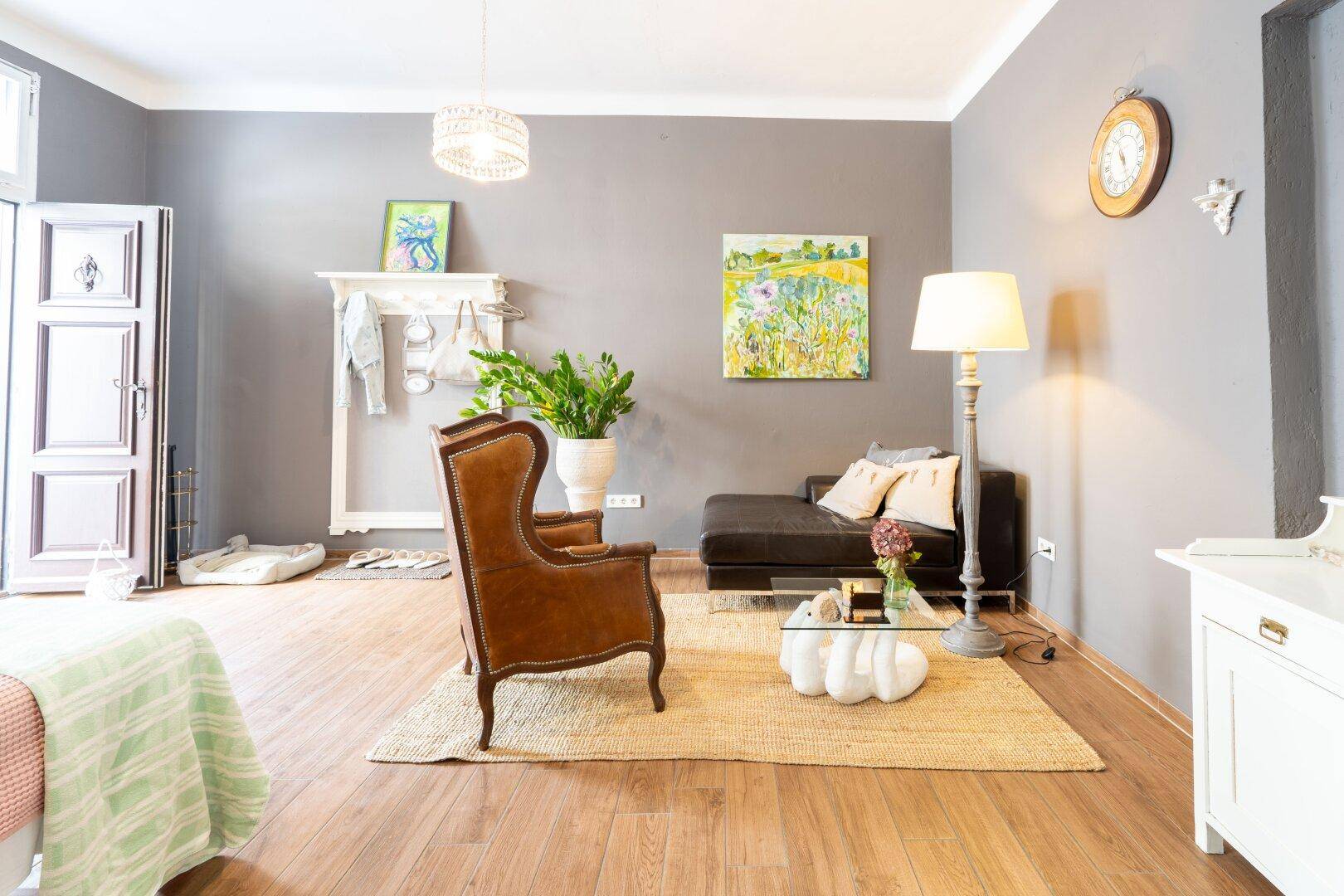 Gemütliches Wohnzimmer mit dunklem Sofa, Sessel und Holzboden, durch große Fenster hell erleuchtet und modern dekoriert.