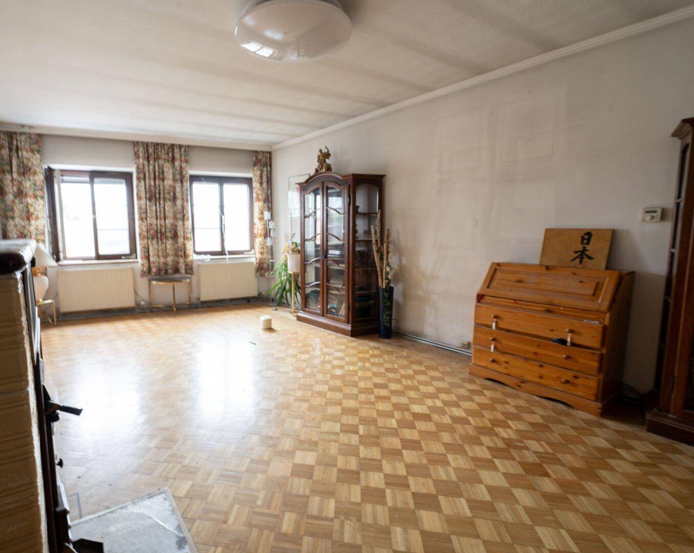 Geräumiges Wohnzimmer mit Parkettboden, floralen Vorhängen und traditionellen Holzmöbeln.