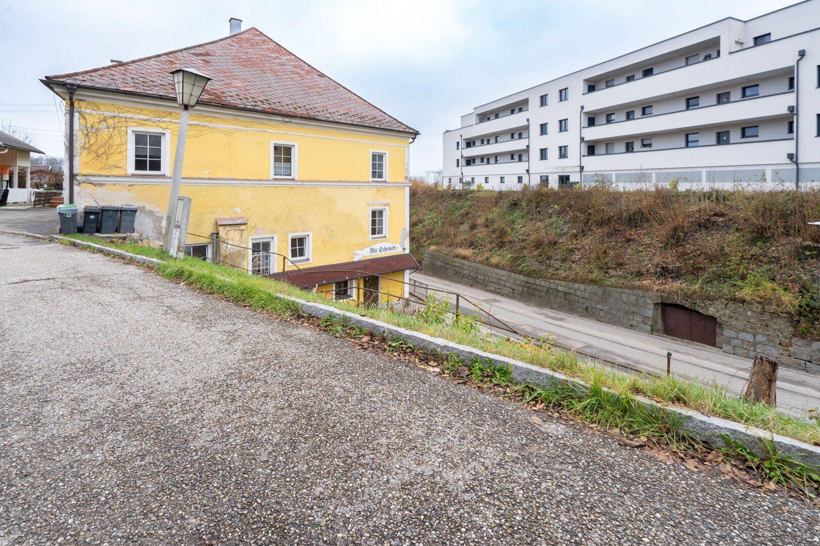 Historisches gelbes Gebäude an einer Straße mit einem modernen Neubau im Hintergrund.