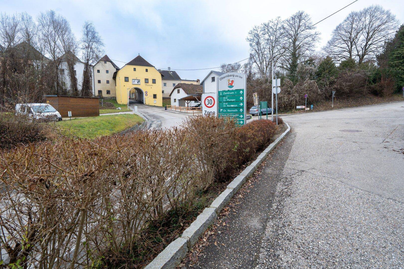 Ländliche Umgebung mit Straßenkreuzung, Wegweisern und historischen Gebäuden in der Ferne.
