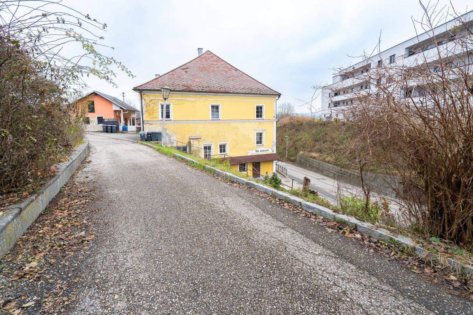 Historisches gelbes Gebäude an einer ansteigenden Straße mit einem modernen Neubau im Hintergrund.
