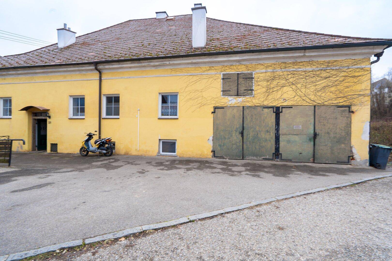 Gelbes historisches Gebäude mit großen Garagentoren und einem Roller davor.