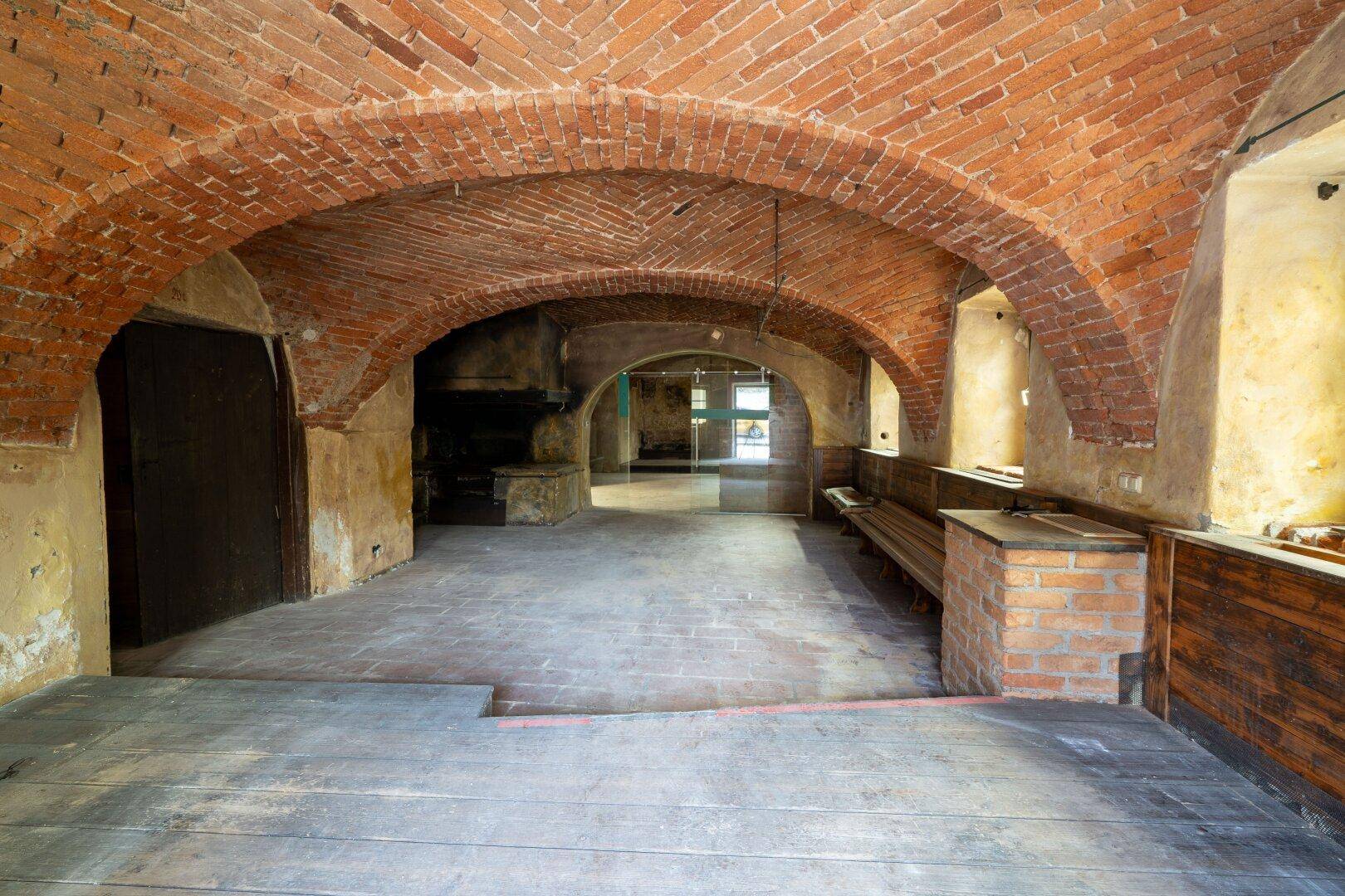 Historischer Gewölbekeller mit Ziegelgewölbe, alten Holzböden und rustikalen Bänken.