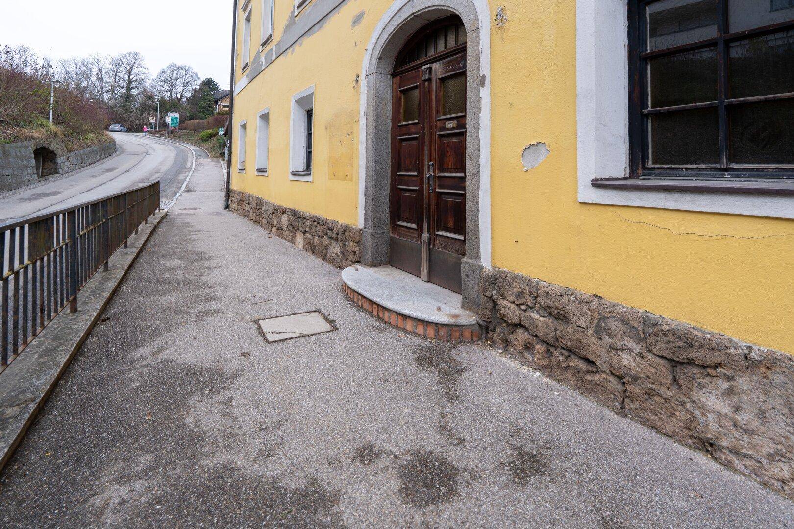 Historisches gelbes Gebäude mit großem Holztor und gepflastertem Gehweg.