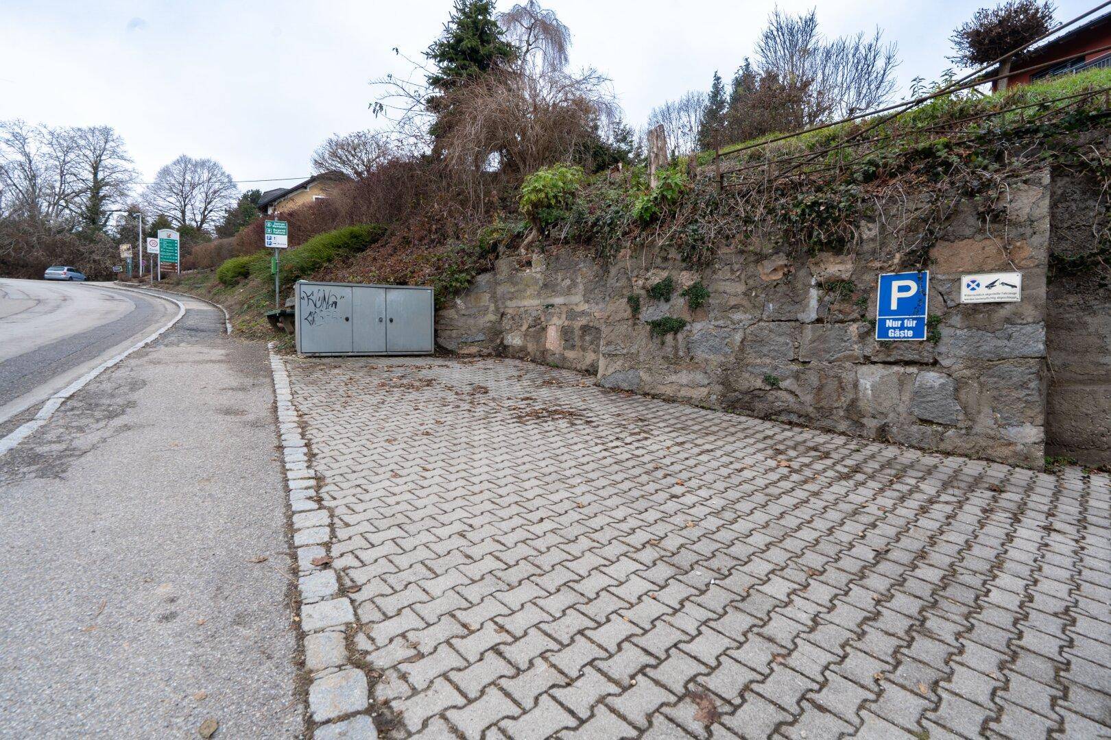Gepflasterter Parkplatz vor einer Steinmauer mit einem Parkschild für Gäste.