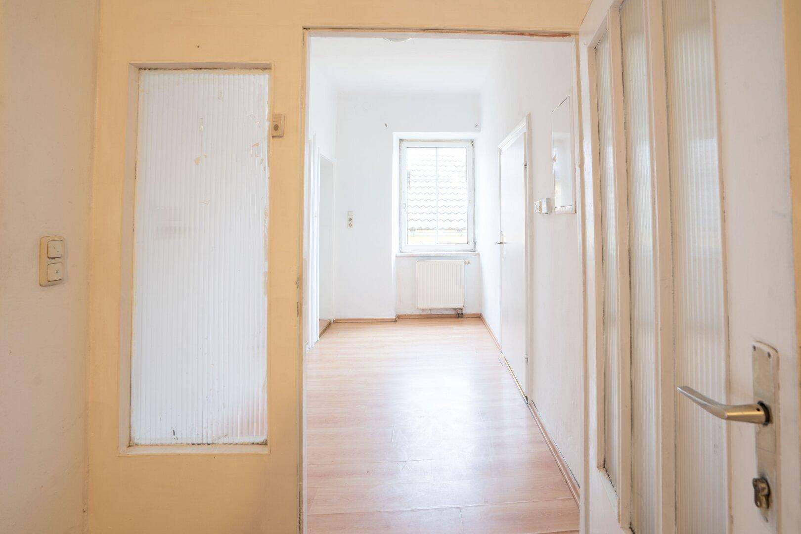 Heller Flur mit Laminatboden und einer Tür mit Glaseinsätzen, die zu weiteren Räumen führt.