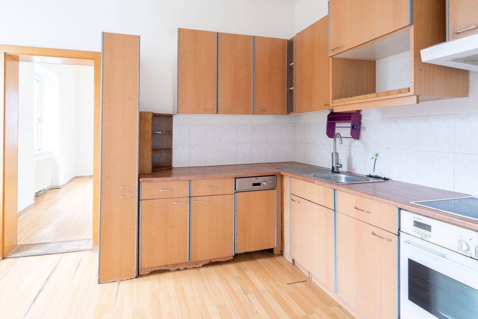 Funktionale Küche mit Holzschränken, Spülmaschine und Blick in einen angrenzenden Raum.