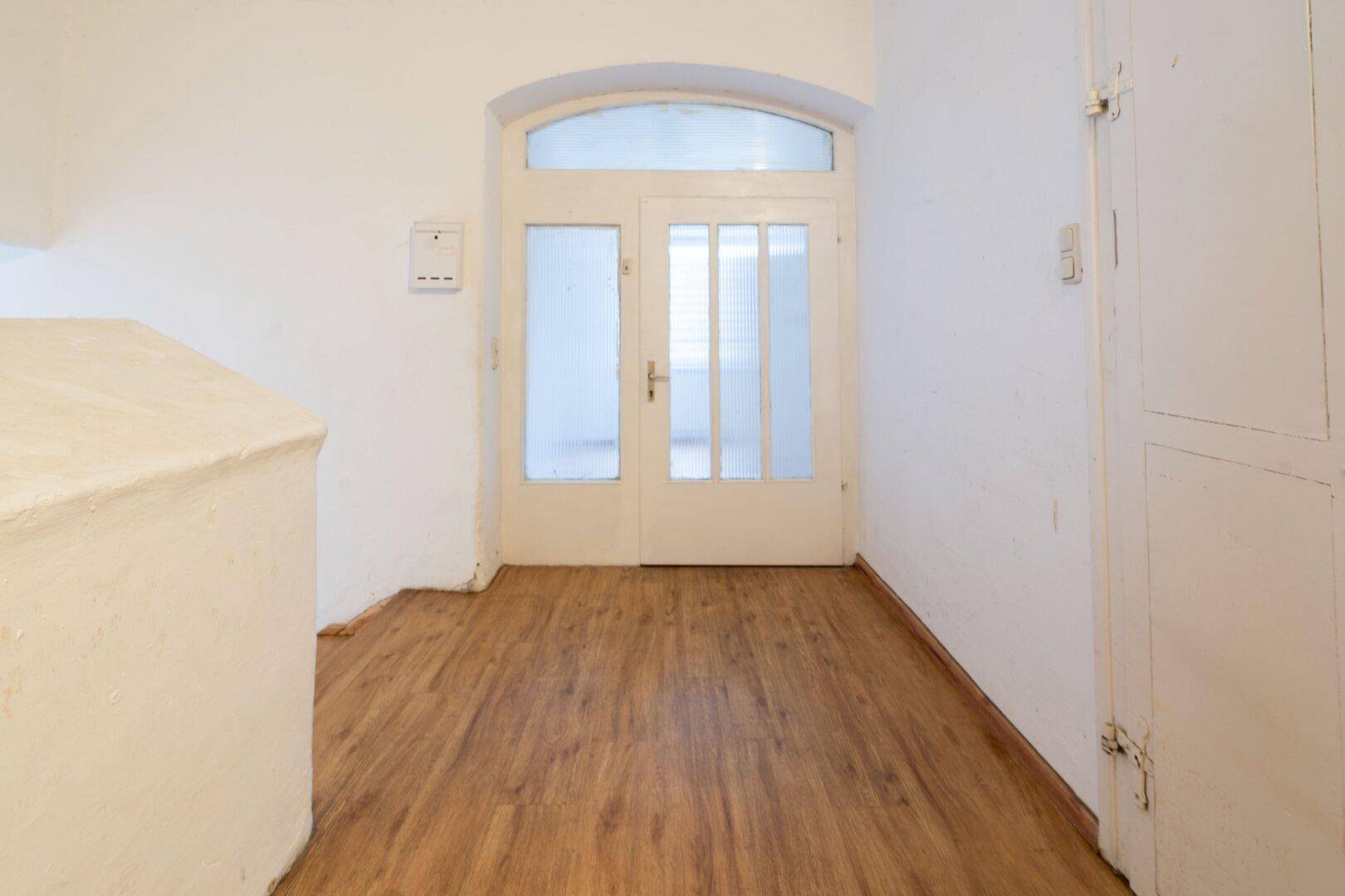 Eingangsbereich mit Holzlaminatboden und einer weißen Doppeltür mit Glaseinsätzen.