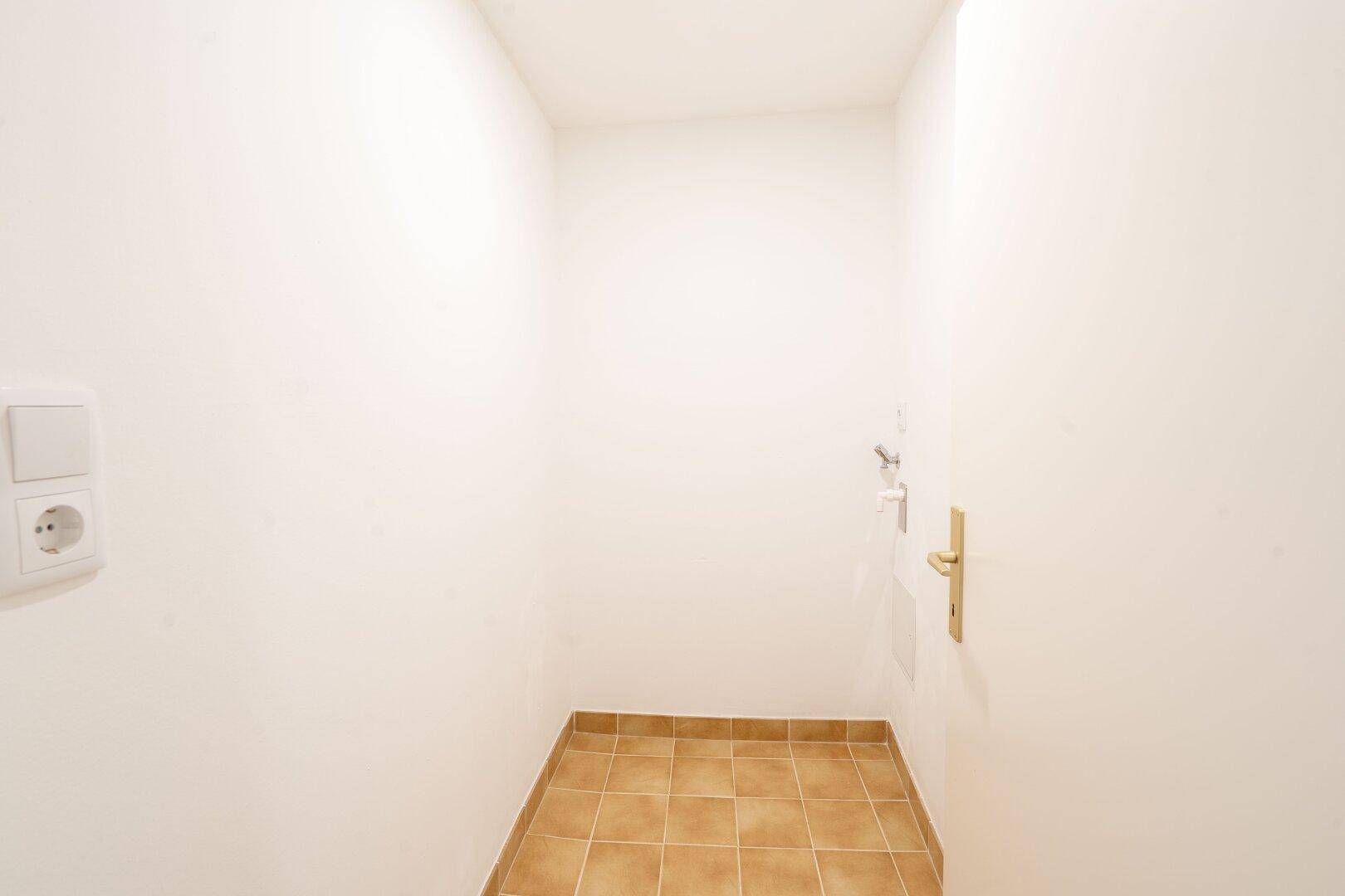 Kleiner Abstellraum mit Fliesenboden und einer Steckdose an der weißen Wand.