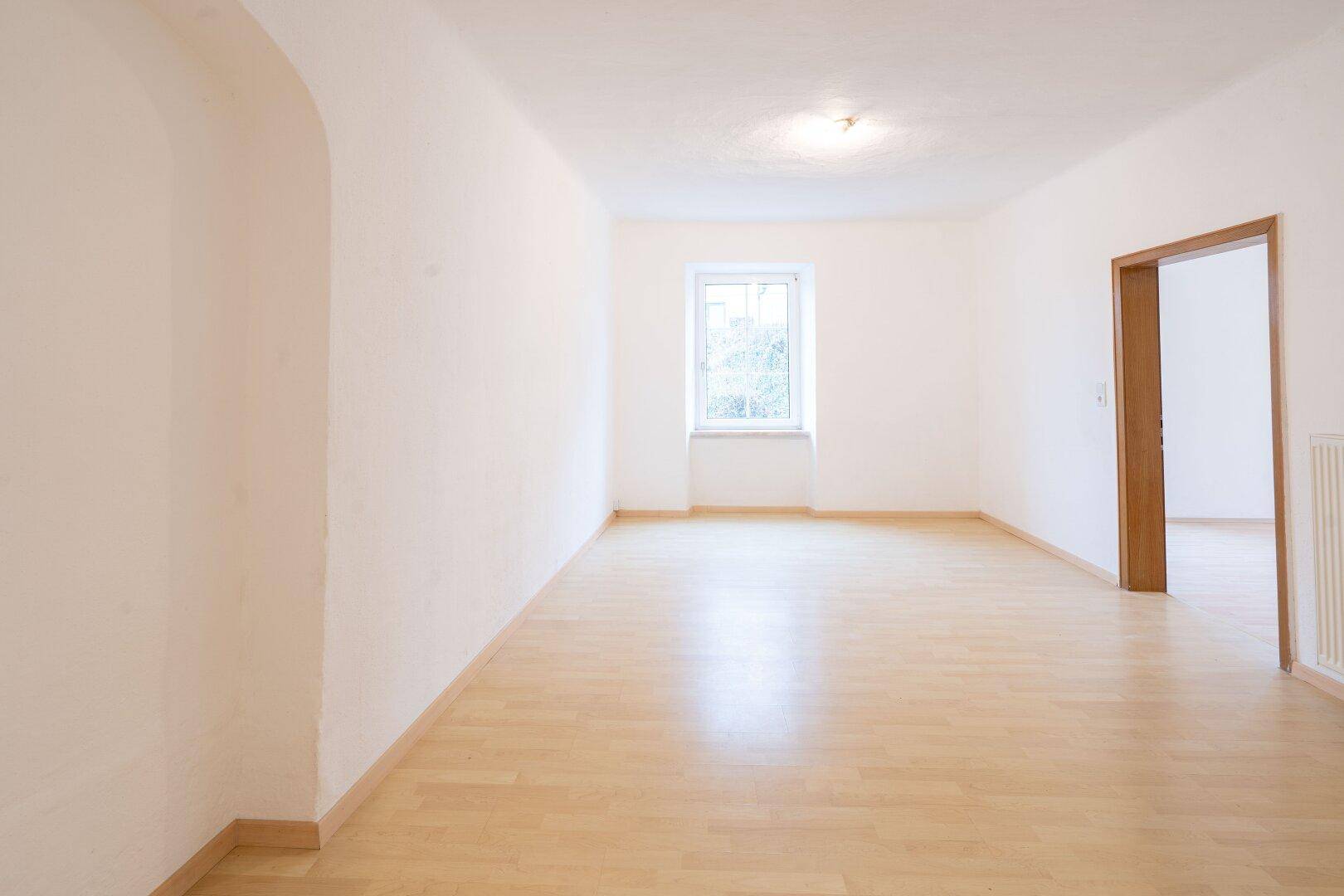 Geräumiges, helles Zimmer mit Holzlaminatboden, weißen Wänden und einem Fenster.