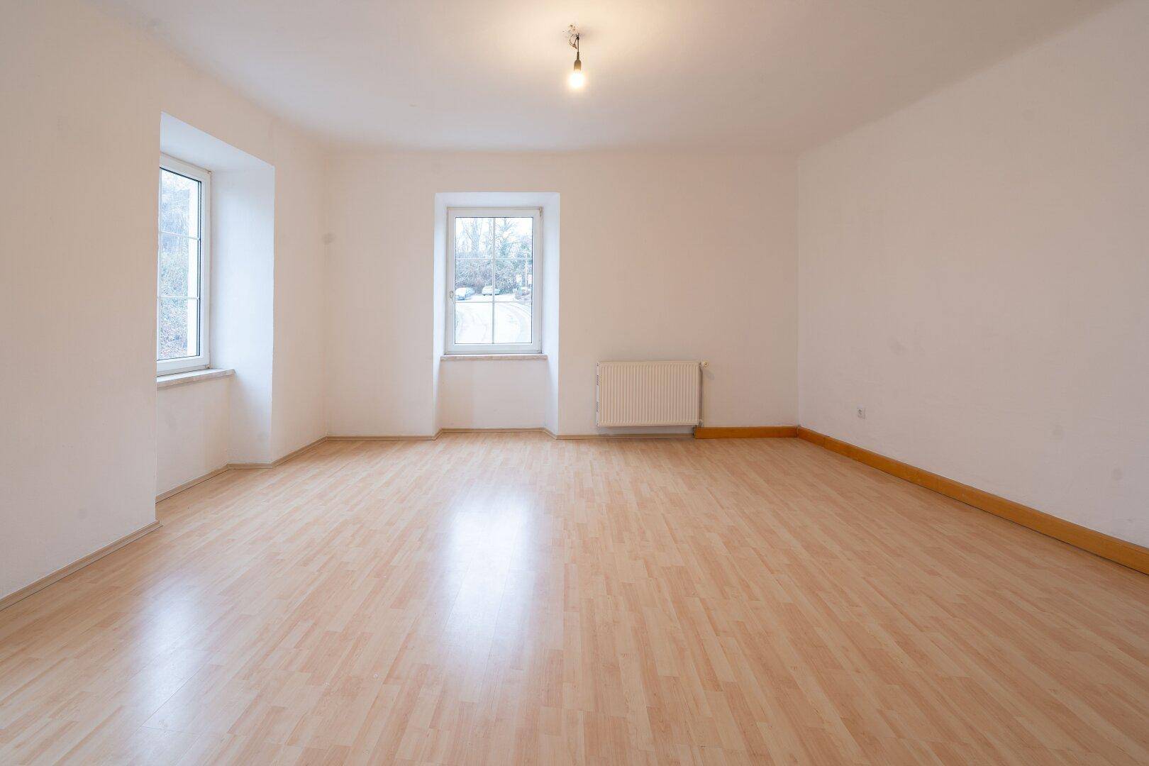Helles Zimmer mit Holzlaminatboden, weißen Wänden und zwei Fenstern.