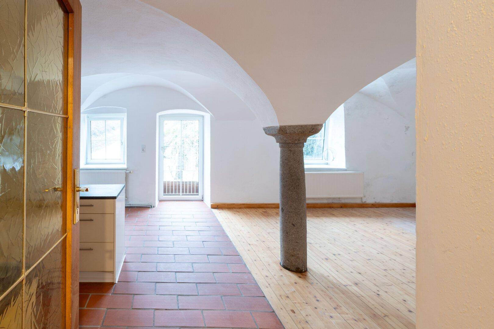 Historischer Raum mit Gewölbedecke, Steinsäule, Terrakottafliesen und Holzdielenboden.