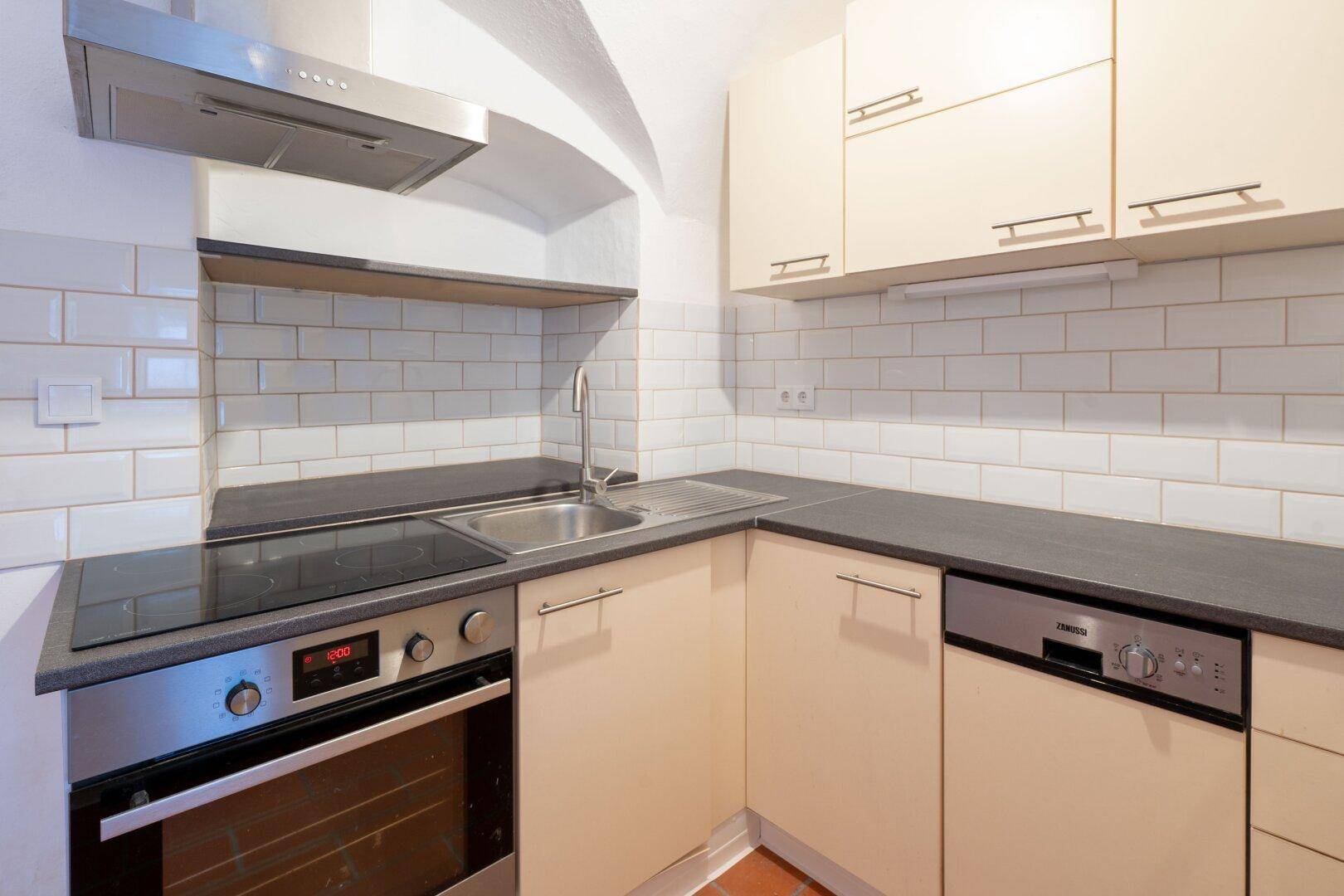 Moderne Einbauküche mit beigen Fronten, Induktionskochfeld, Backofen und Spülmaschine.