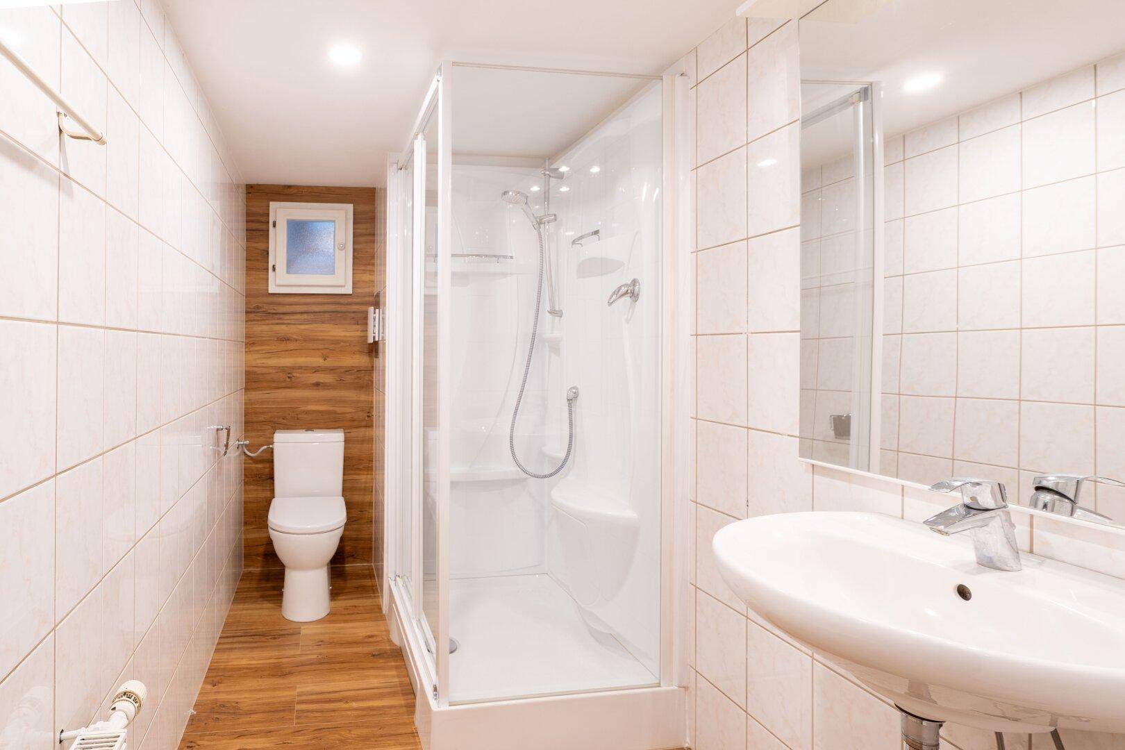 Modernes Badezimmer mit Duschkabine, WC, Waschbecken und Fliesen in Weiß und Holzoptik.