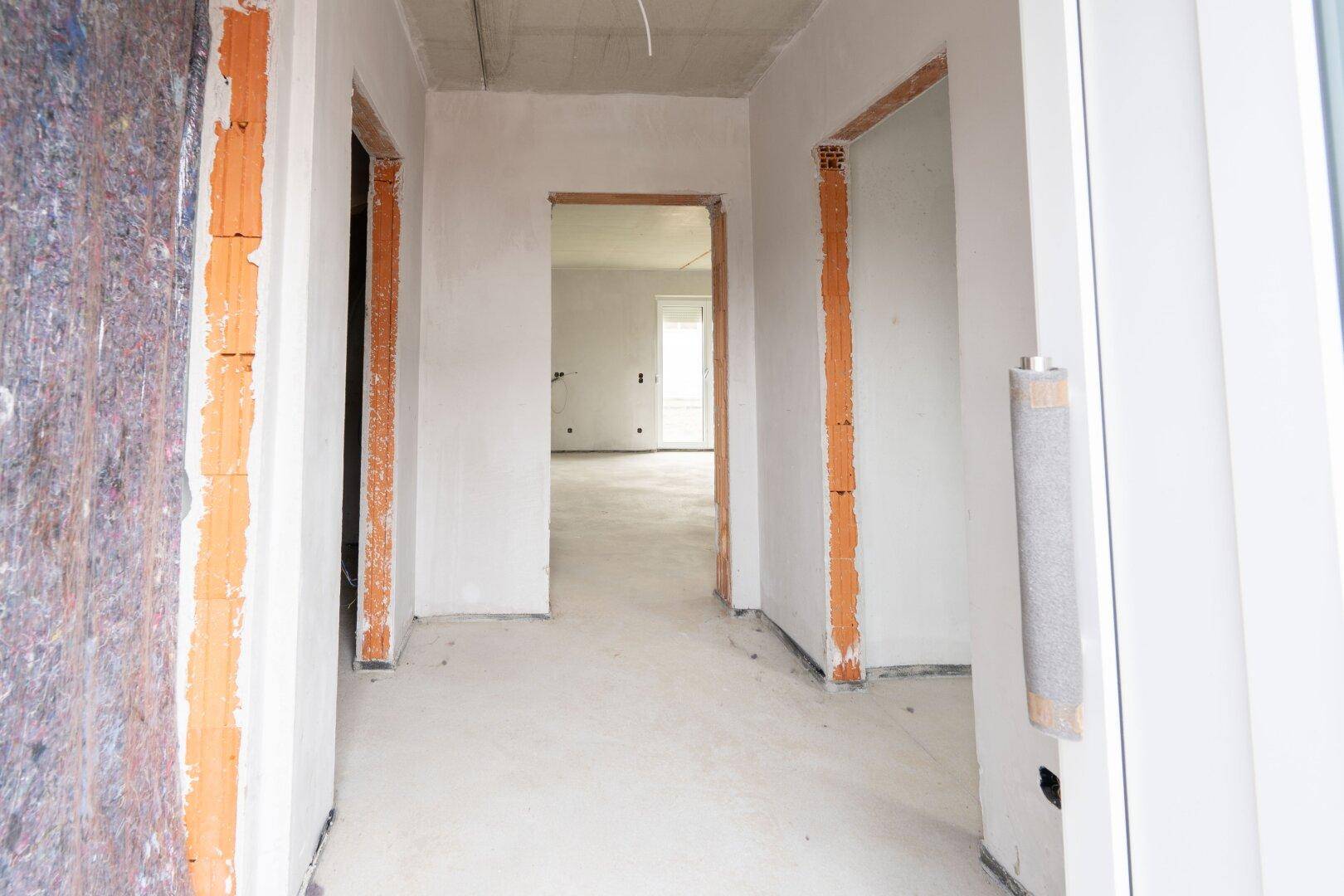 Unfertiger Flur im Rohbauzustand mit unverputzten Türrahmen und Betonboden.