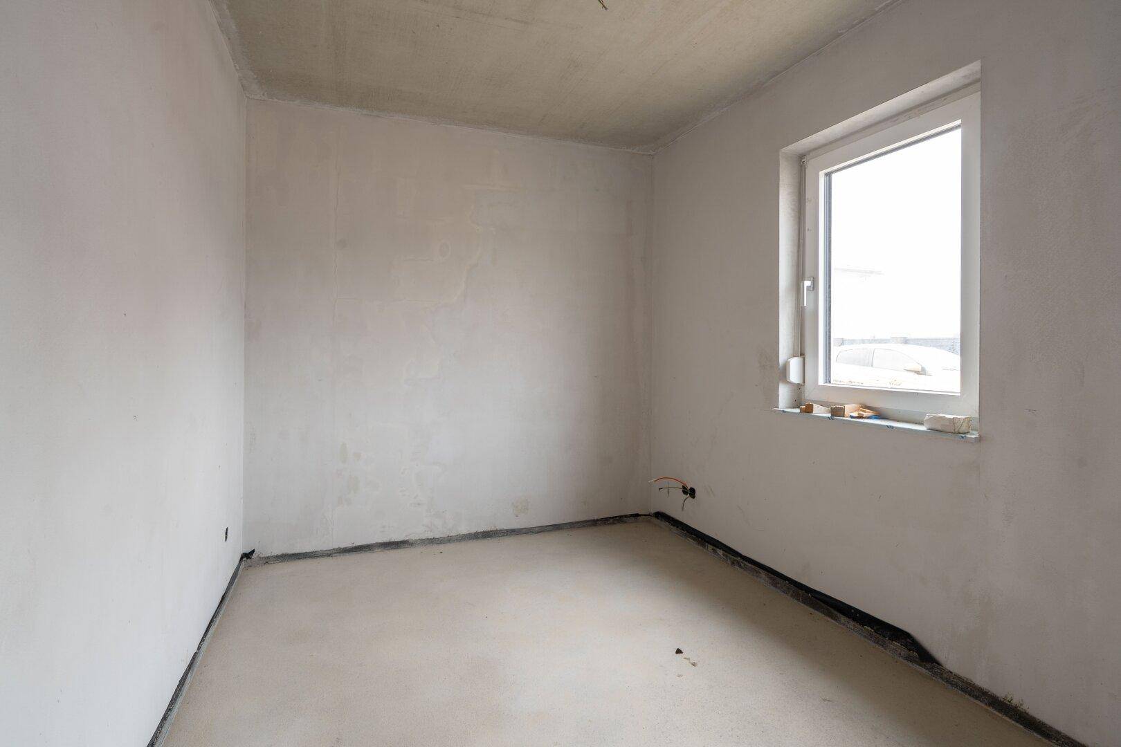Leerer Raum im Rohbau mit Fenster, unverputzten Wänden und Betonboden.
