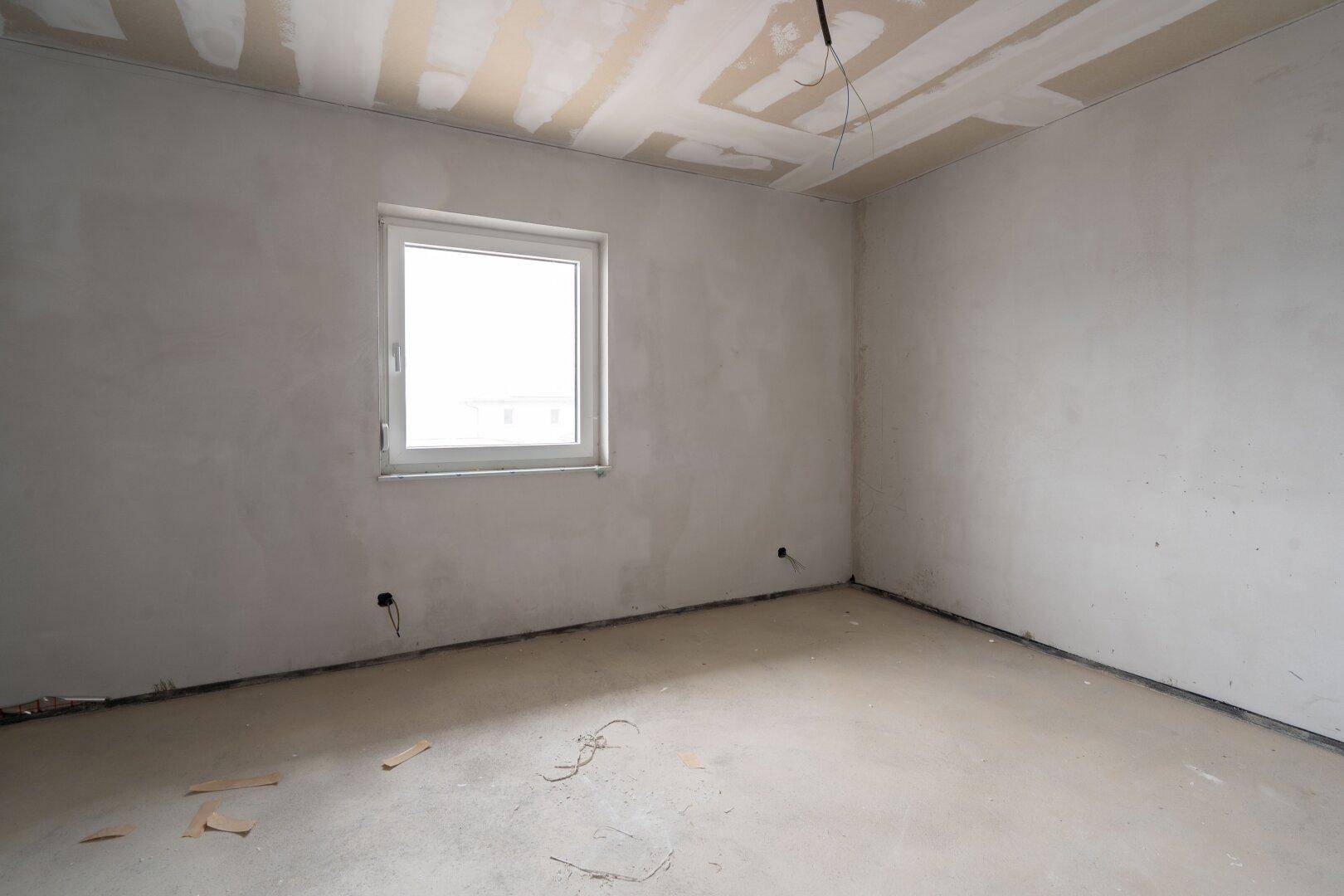 Leerer Raum im Rohbau mit Fenster, unverputzten Wänden und Betonboden.