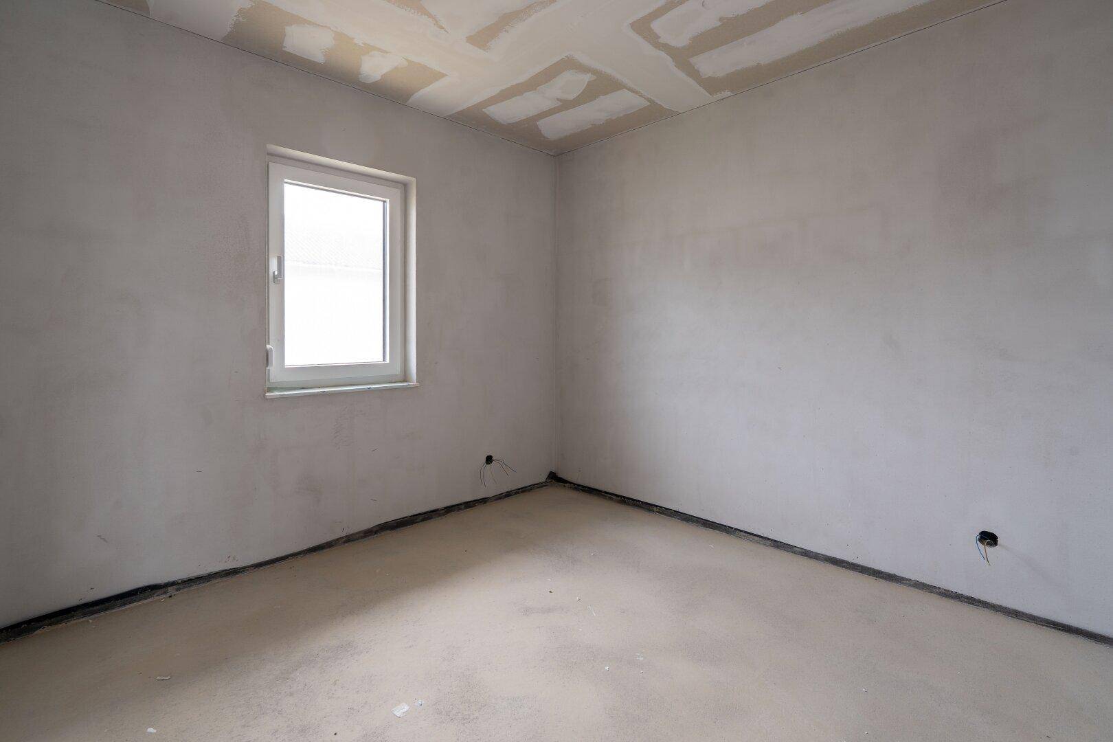 Leerer Raum im Rohbau mit Fenster, unverputzten Wänden und Betonboden.