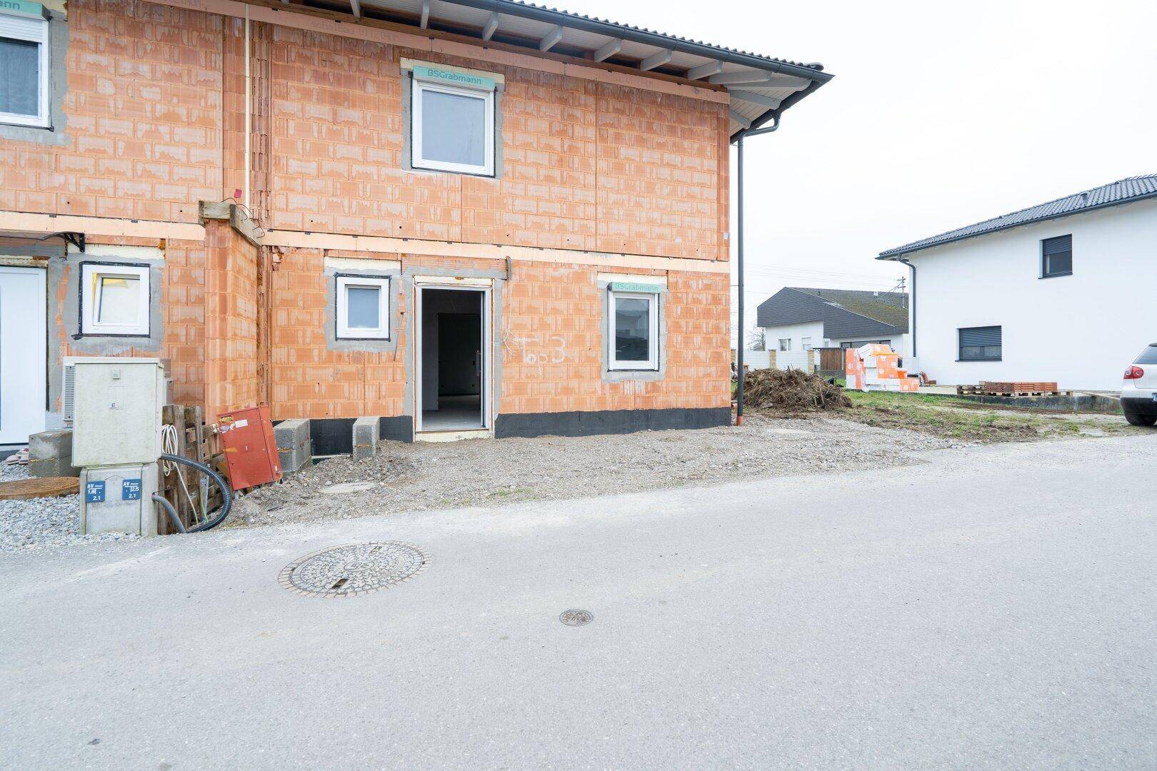 Seitenansicht der Doppelhaushälfte im Rohbau mit Baustelle und angrenzender Straße.