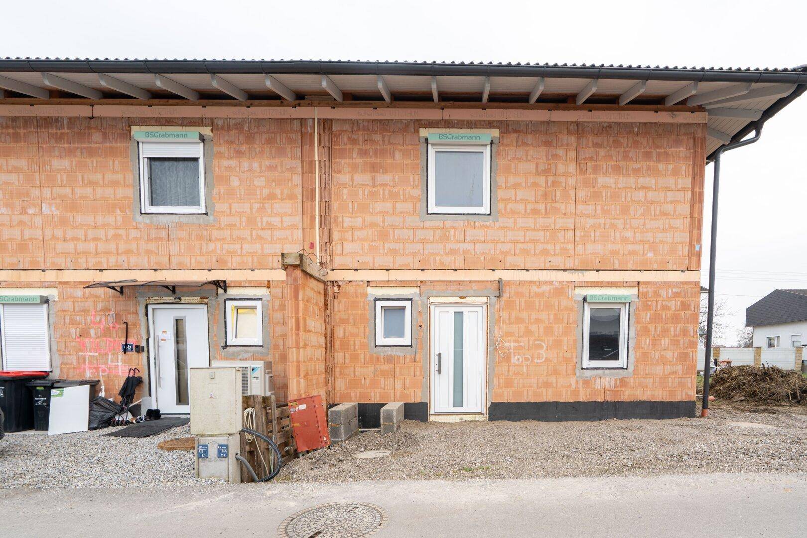 Neubau-Doppelhaushälfte im Rohbauzustand mit sichtbaren Ziegelwänden und Fenstern.