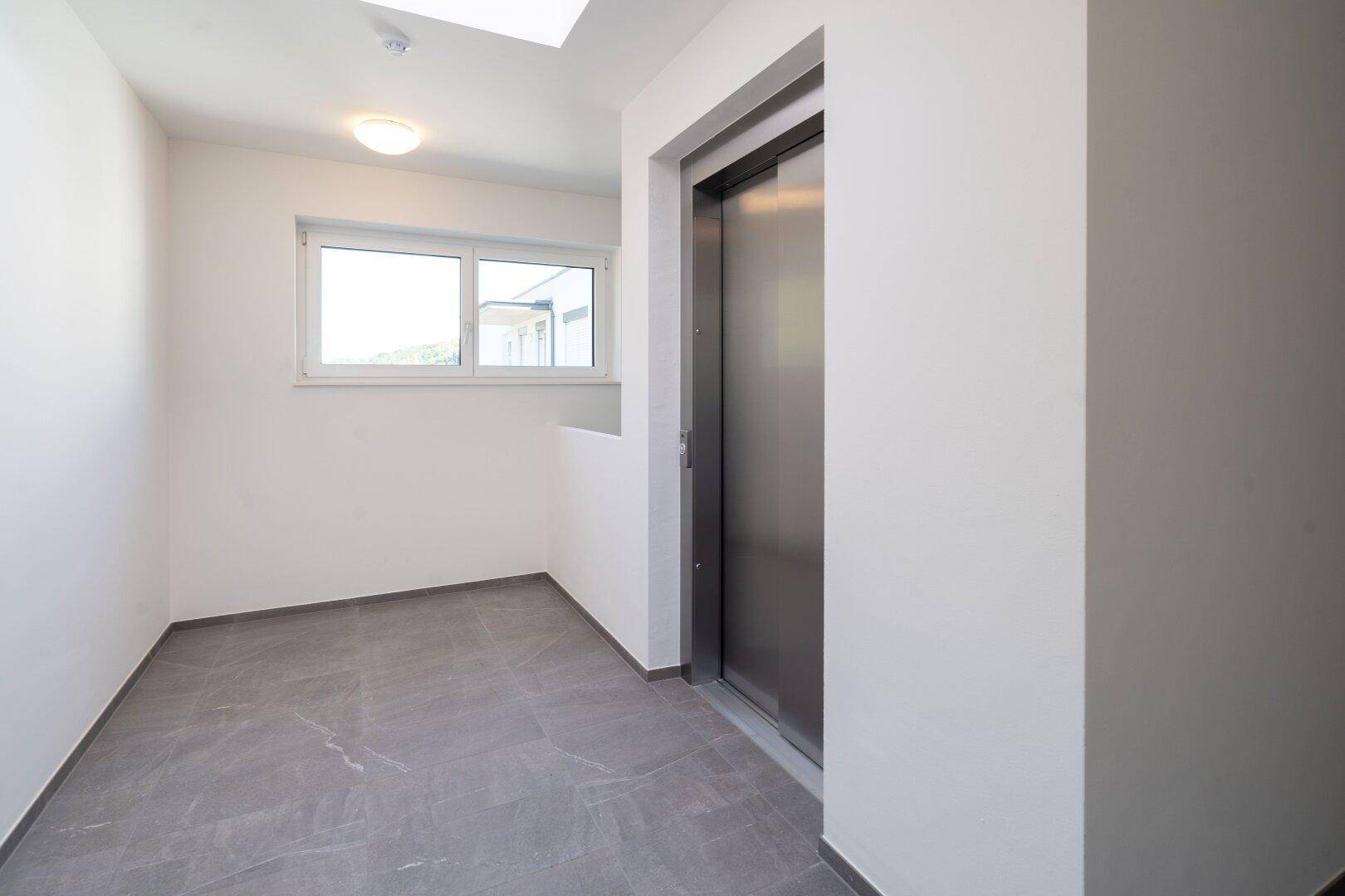 Heller Flurbereich im Obergeschoss mit Aufzug, Fenster und Oberlicht für viel Tageslicht.