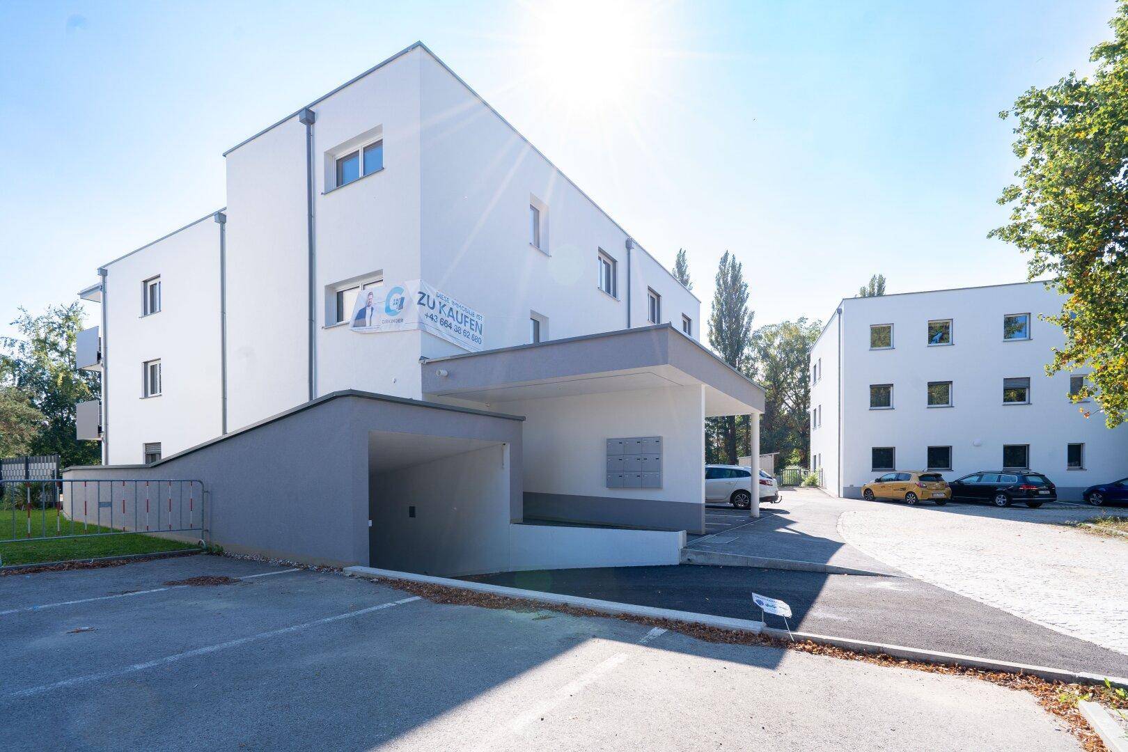 Moderner Wohnkomplex mit Tiefgaragenzufahrt, Außenparkplätzen und sonniger Umgebung.