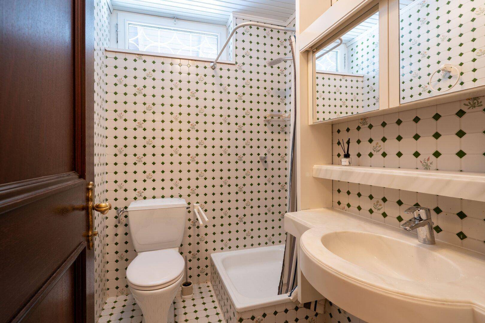 Kleines Badezimmer mit Dusche, WC und gemusterten Fliesen, funktional und hell.