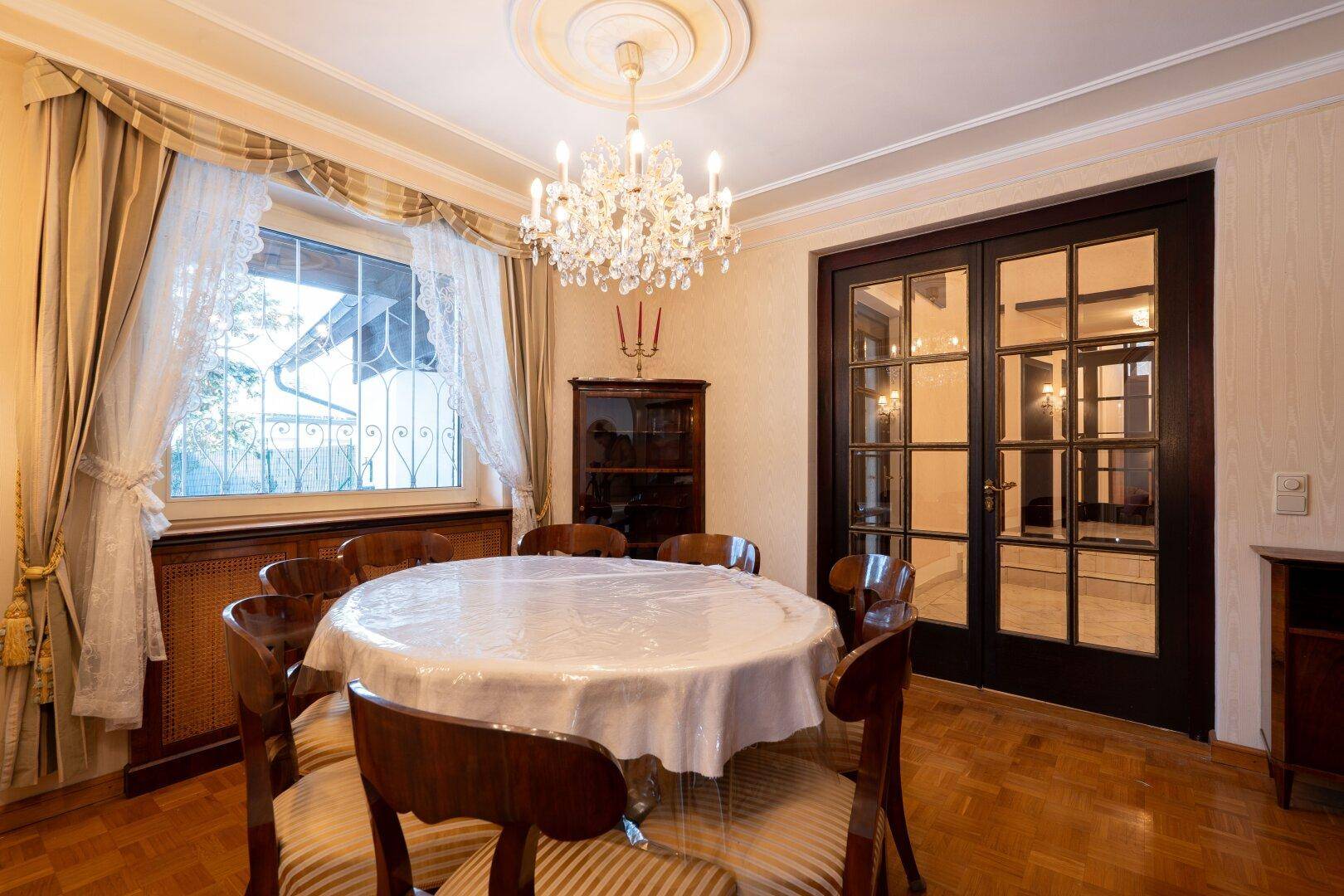Klassisches Esszimmer mit Parkett, Kronleuchter und Blick durch das Fenster, das viel Licht spendet.